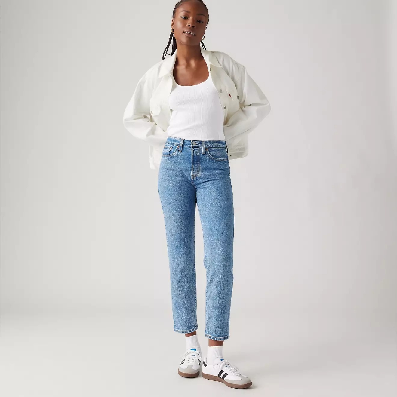 Person in a white top, light jacket, and jeans, wearing sneakers, posing casually