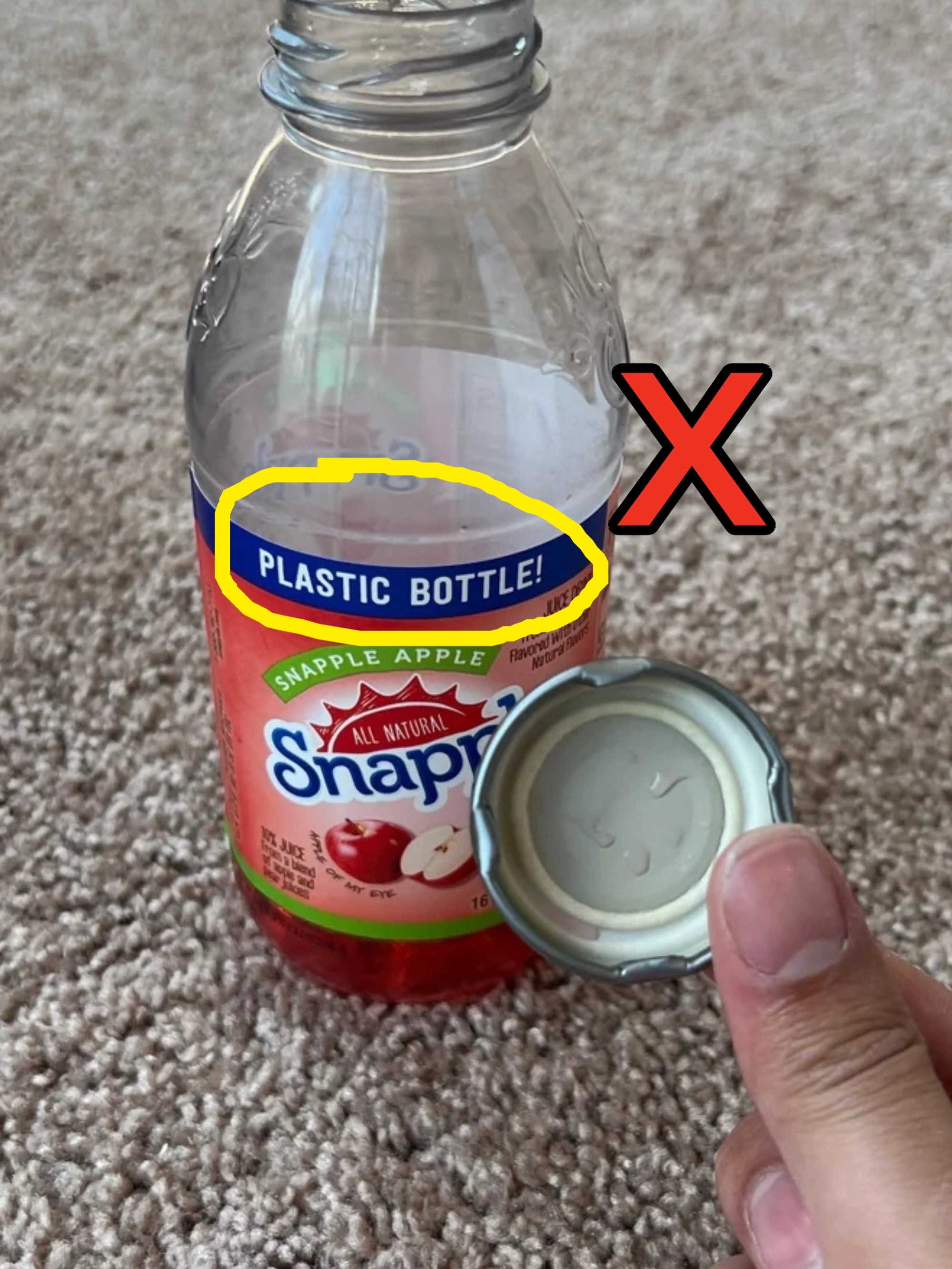 A hand holds the lid of an open Snapple plastic bottle on a carpeted floor