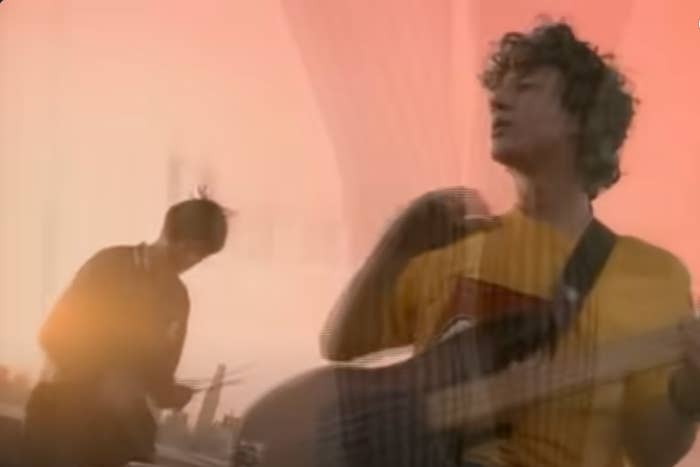 Two musicians playing instruments with a blurred, creator overlay; 1 plays guitar, the different drums