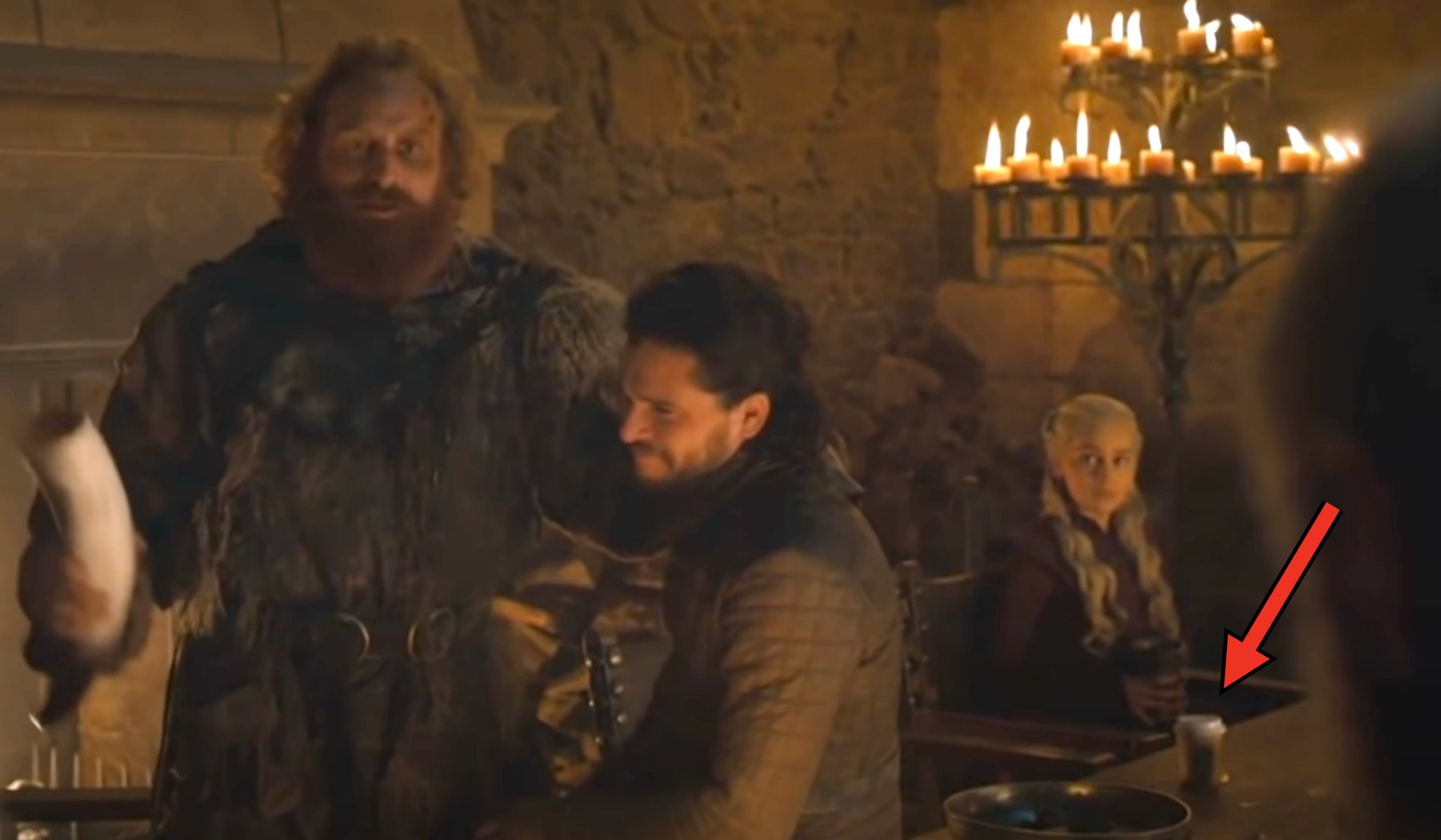 Jon, Tormund, and Daenerys in a stone hall with candles; next to Daenerys is a coffee cup