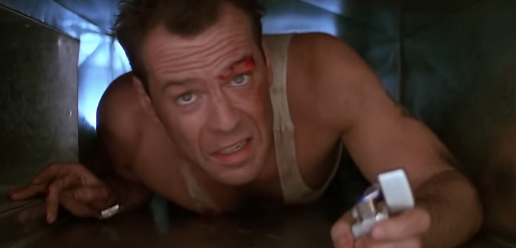McClane crawling through a ventilation duct, holding a lighter in one hand