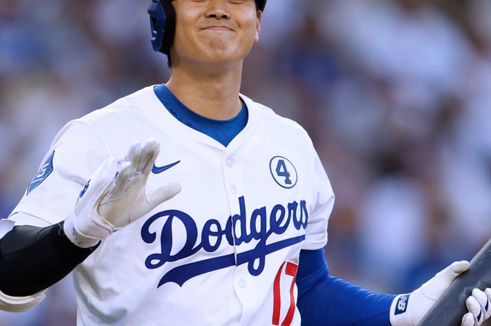 バッターボックスでバットを持つ野球選手。ドジャースのユニフォームを着て微笑み、試合中の一場面。