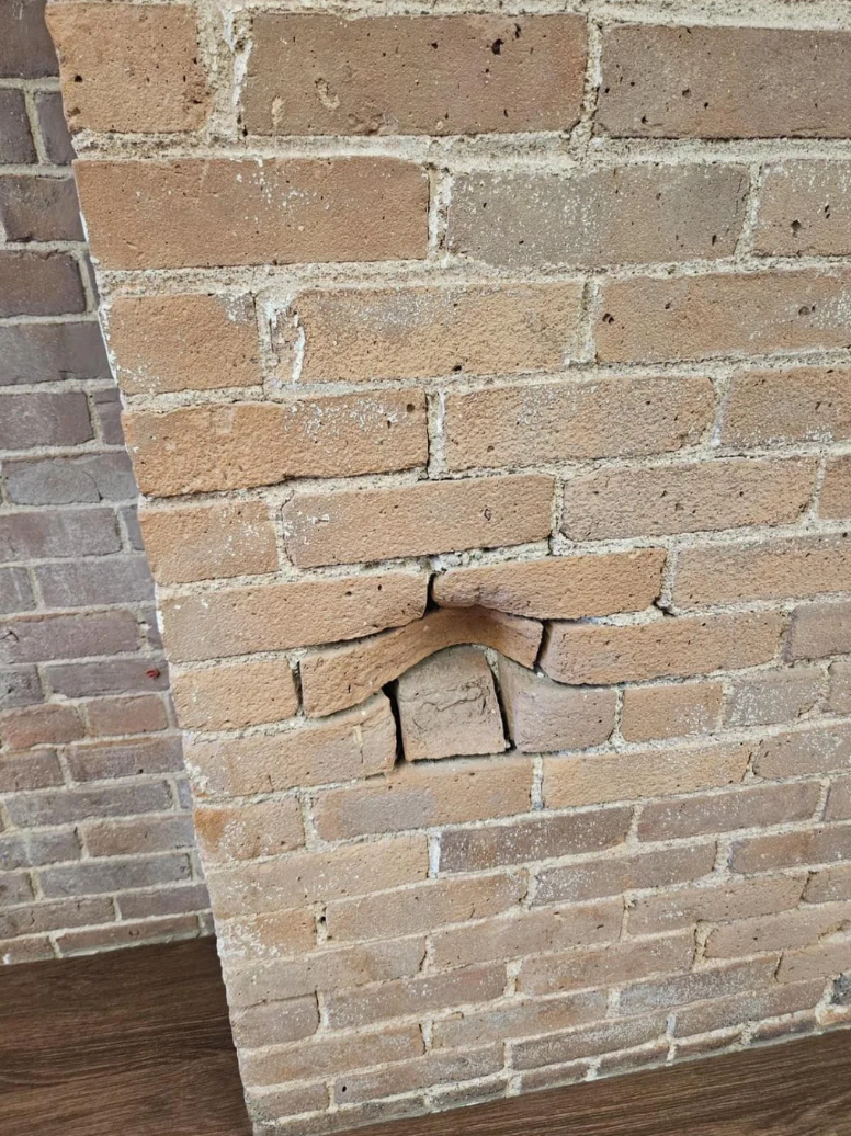 Brick wall with one brick protruding, giving the appearance of a small roof shape