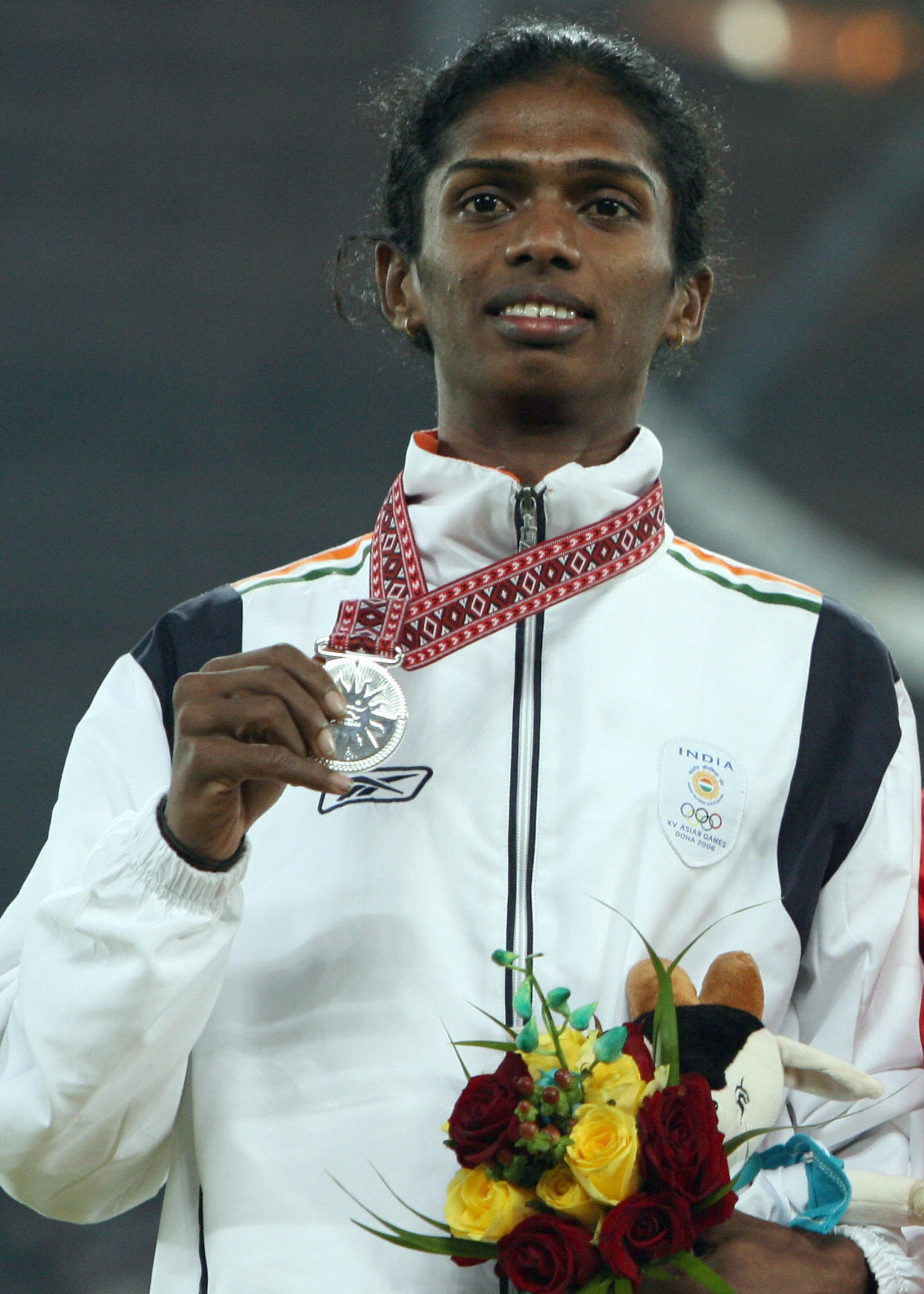 Athlete holding a silver medal and flowers, wearing a sports tracksuit with an Olympic logo, symbolizing achievement and celebration