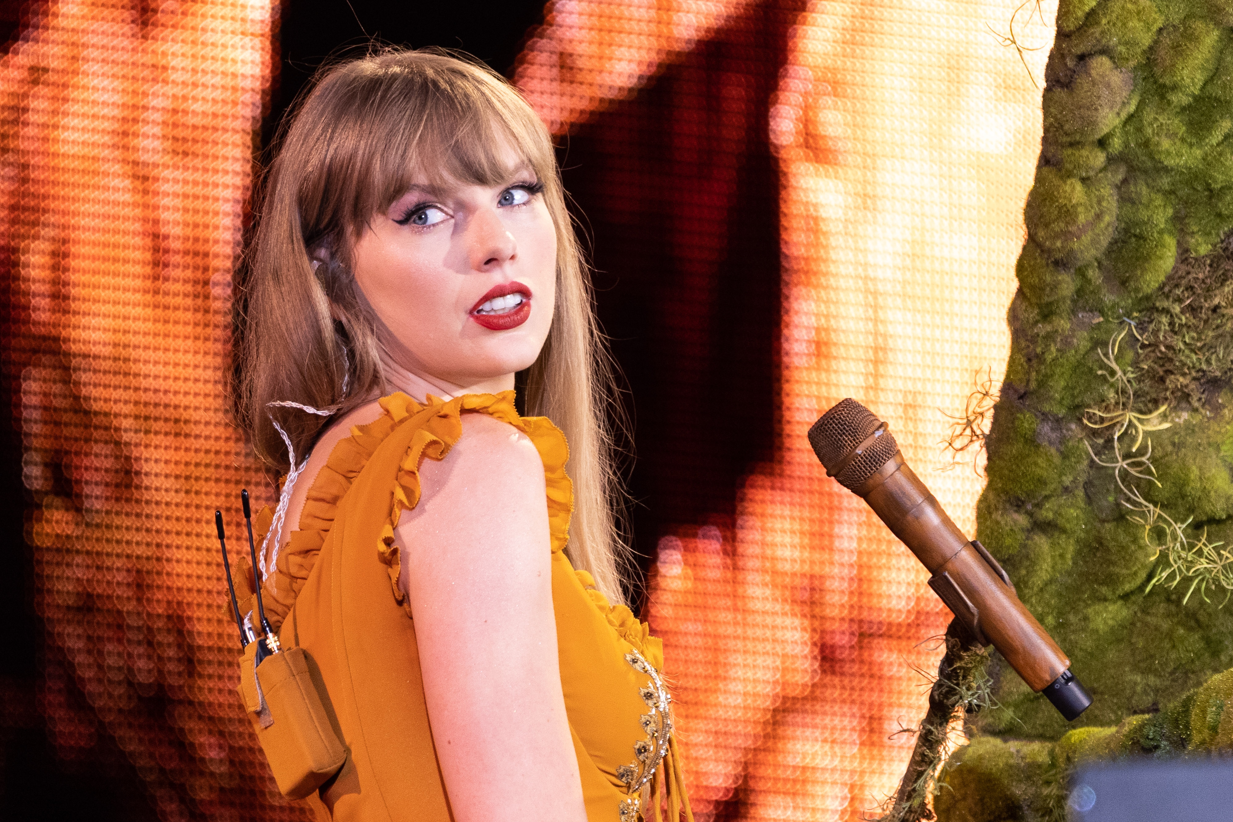 Taylor Swift performs on stage, wearing a ruffled dress and holding a microphone