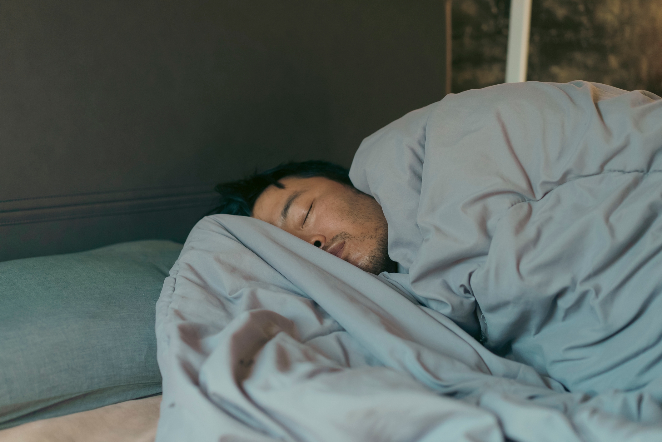 Personen som sover godt i sengen, pakket inn i et teppe, hviler på en pute. Ansiktsuttrykket deres er fredelig og avslappet