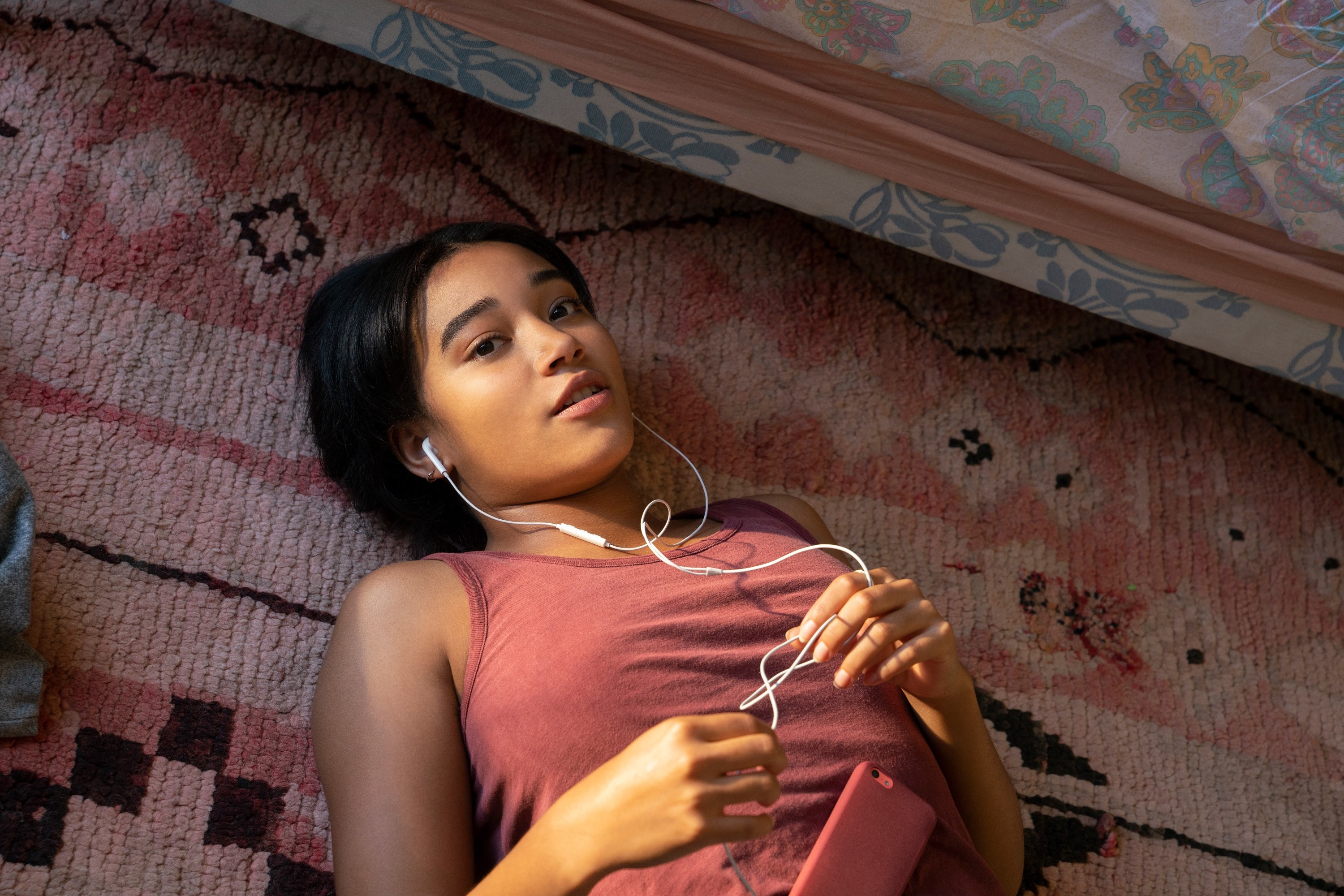 Person lying on a patterned rug, wearing earphones and holding a phone