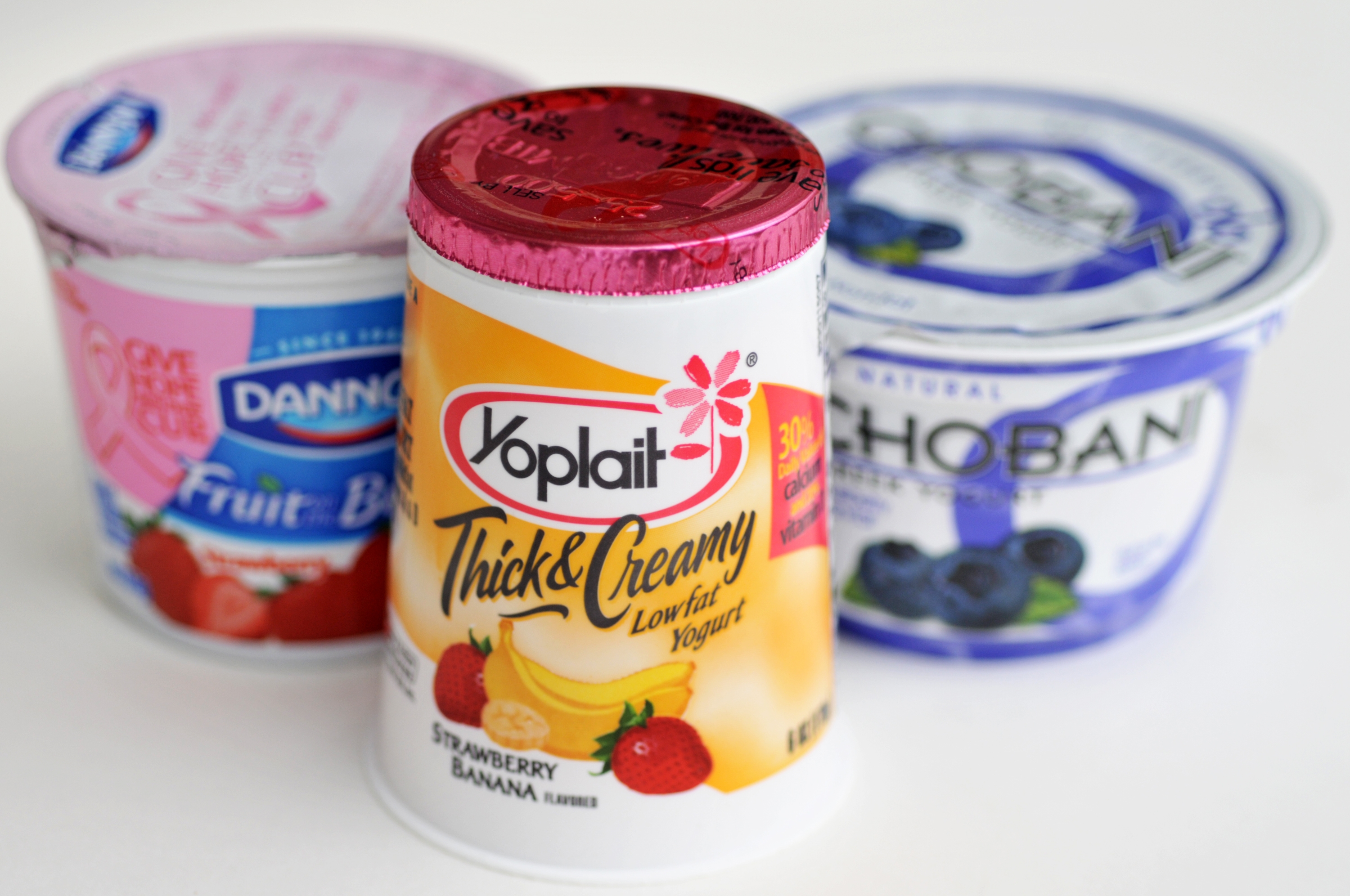 Tre yoghurtbeholdere: Yoplait tykk & amp; amp; Kremet jordbærbanan foran, Dannon -frukt på bunnen, og Chobani Blueberry