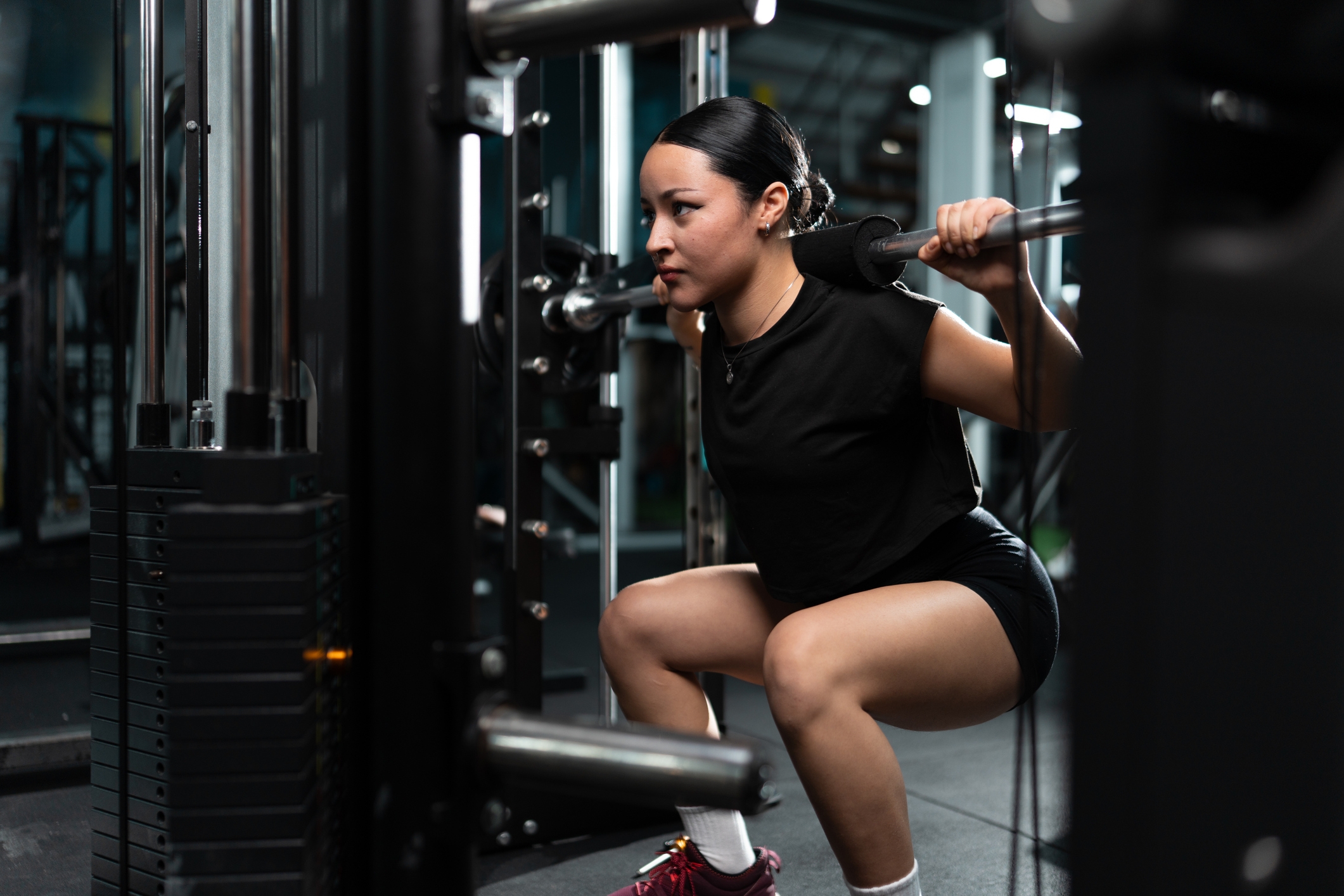 Person som har treningsantrekk og utfører en knebøy med vektstang i et treningsmiljø