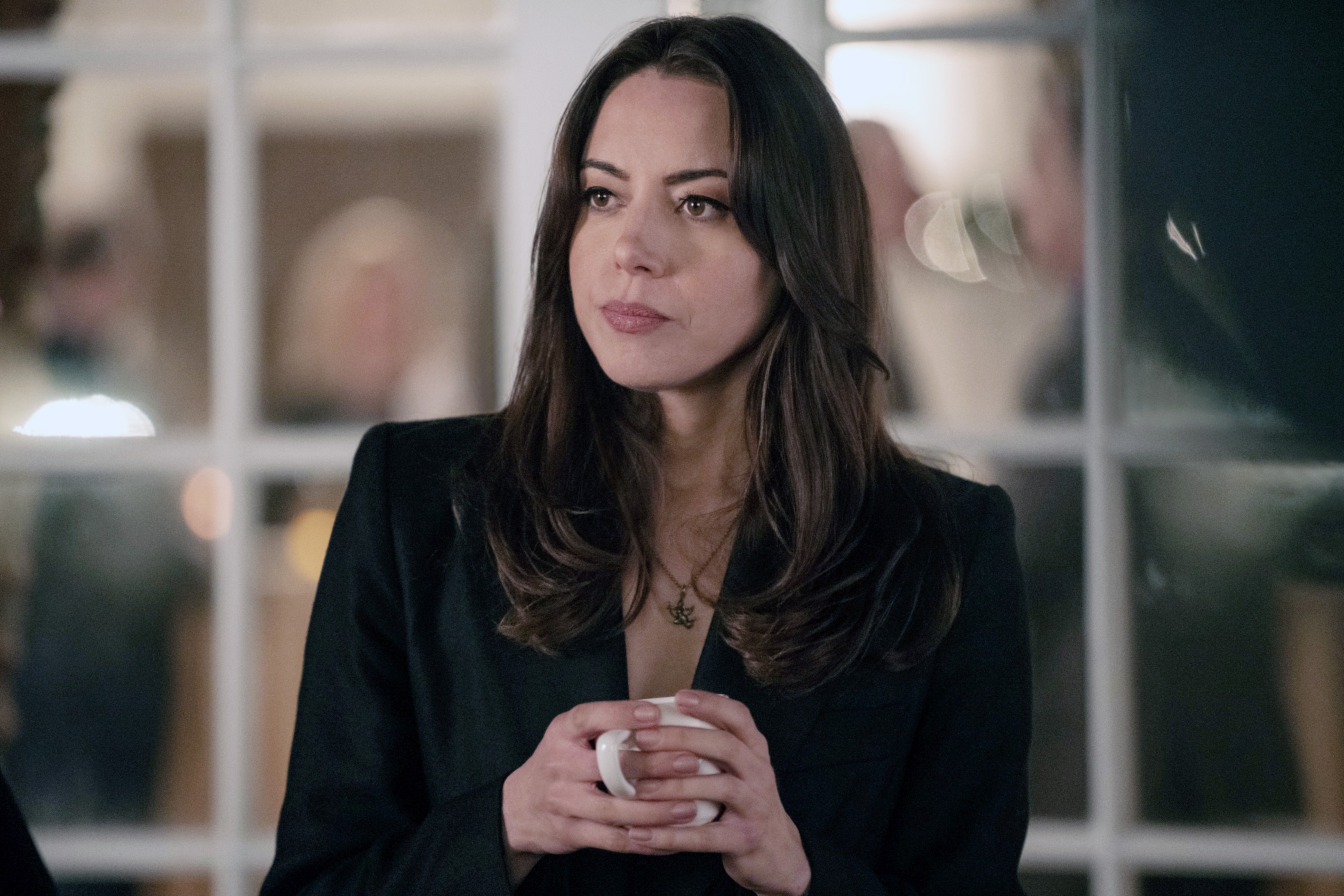 Person holding a mug, wearing a dark jacket, looking thoughtful in an indoor setting