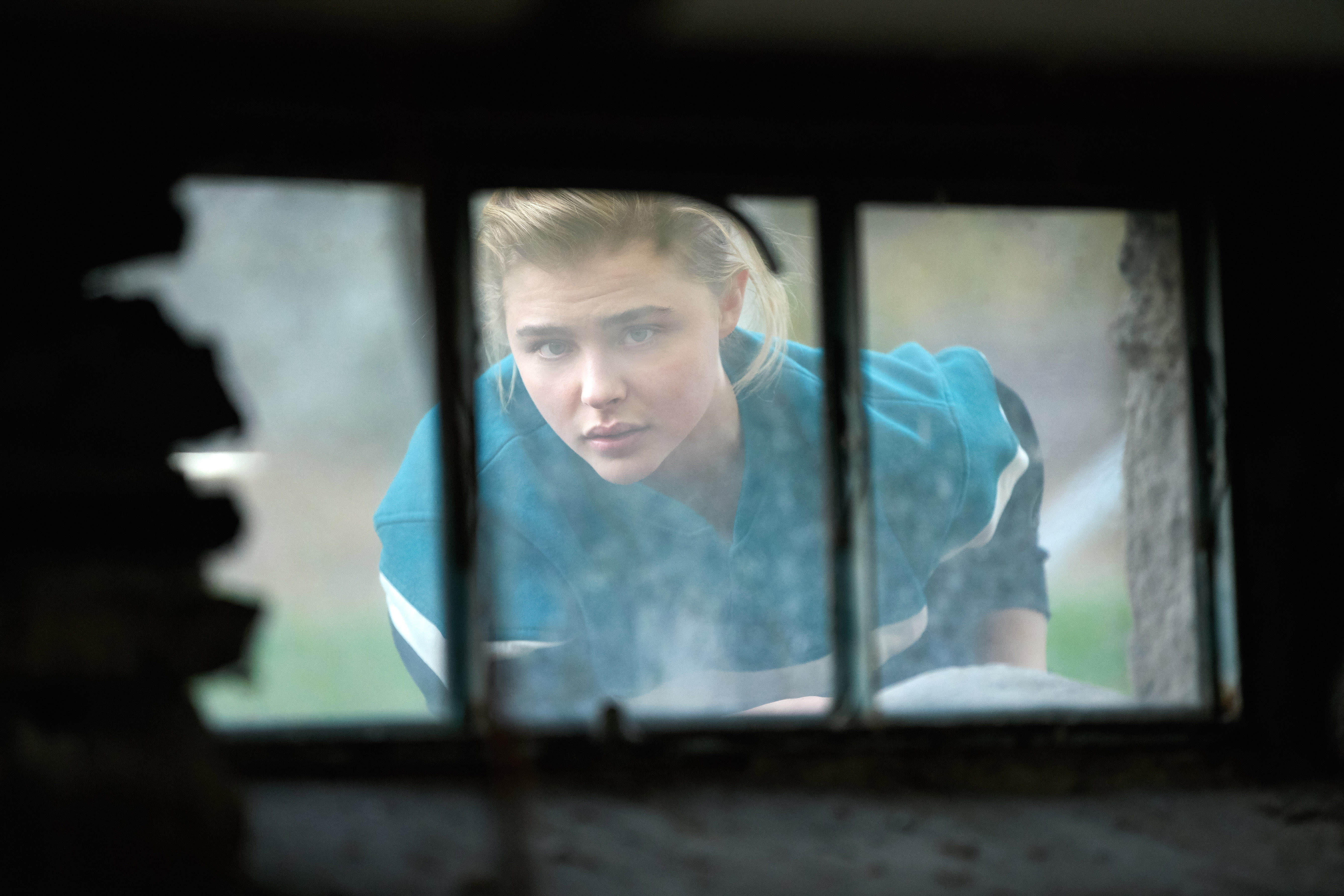 Person looking through a window, wearing a casual jacket, appearing contemplative