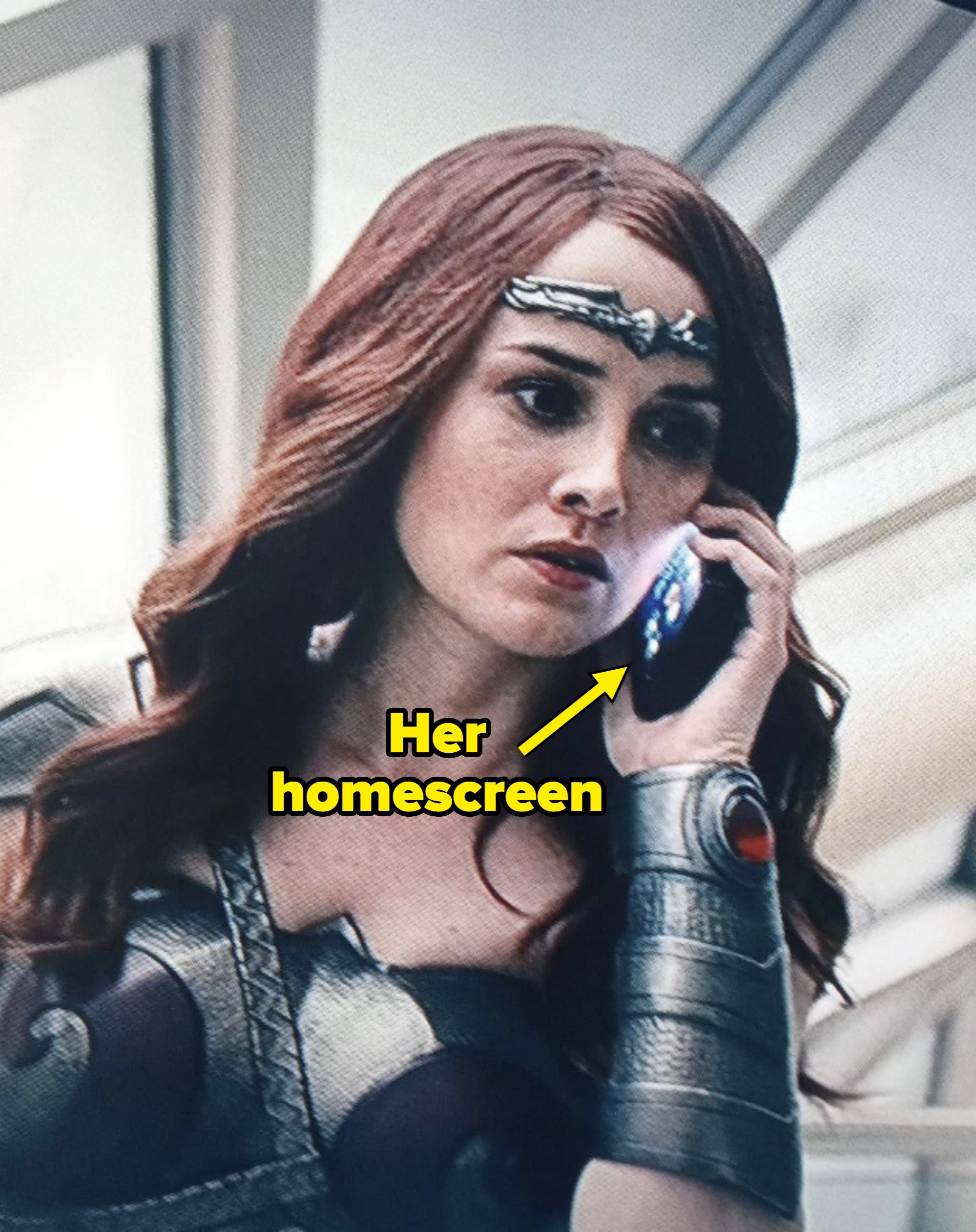 Maeve holding a phone to her ear. You can see her homescreen on the phone