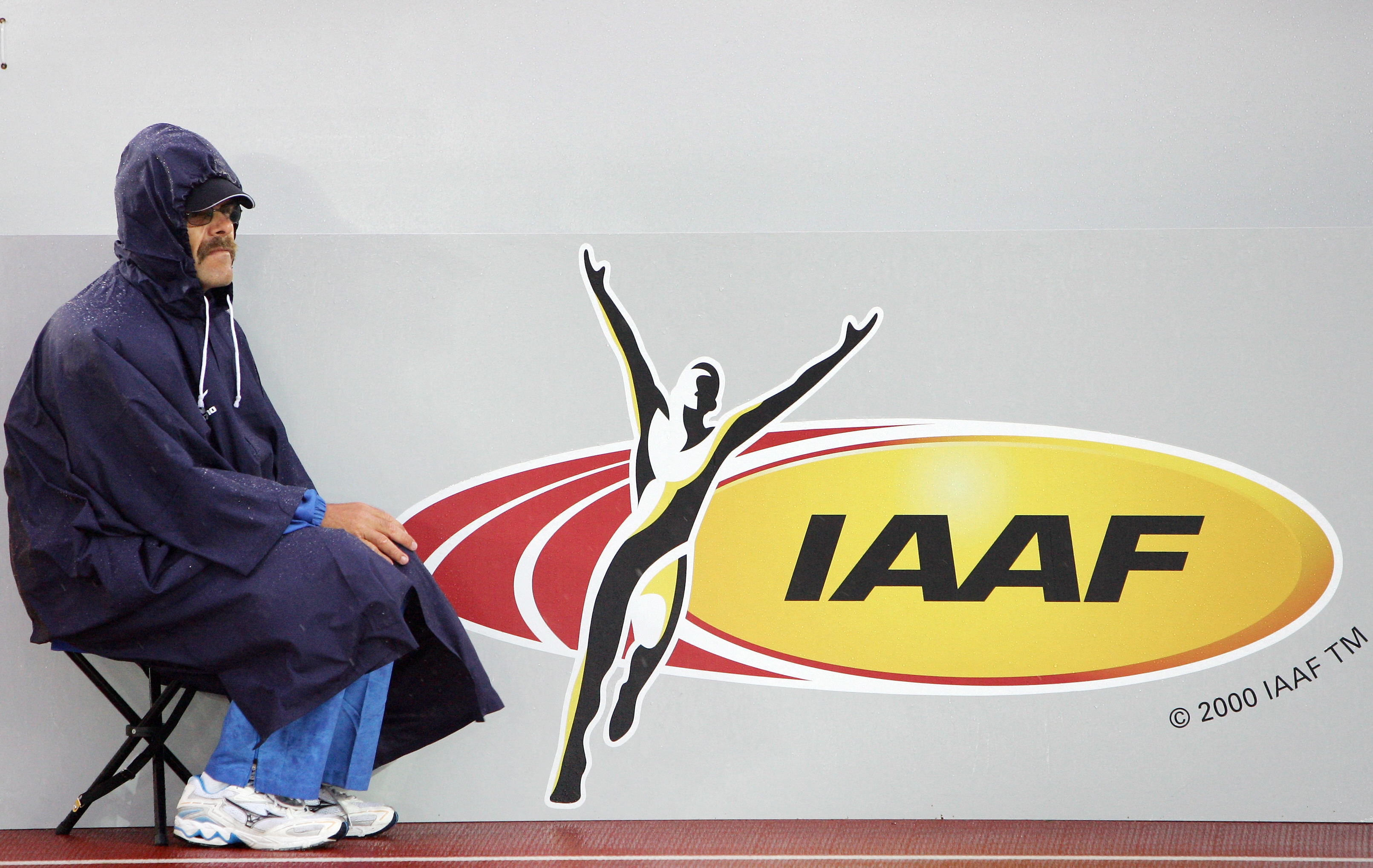 Person in a hooded coat sits on a folding chair beside an IAAF logo, which features a running figure