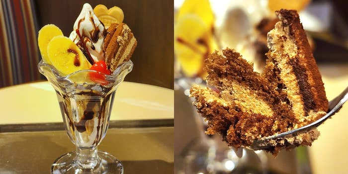 デザートパフェにクリーム、サクランボ、チョコシロップがのり、隣にチーズケーキがフォークに刺さっています。