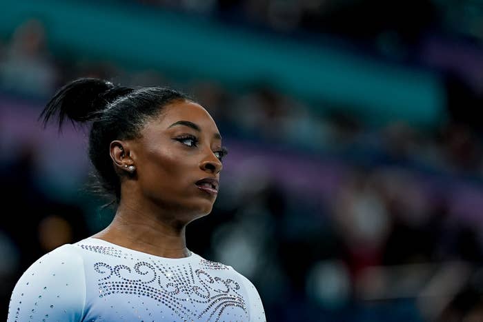 Simone Biles in a detailed leotard, looking focused at a sporting event