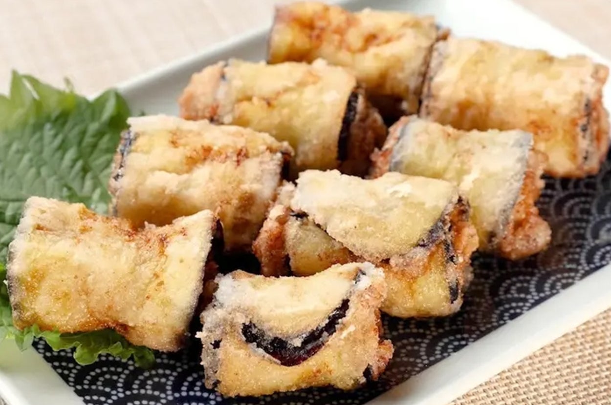 揚げ物料理が白い皿に盛られており、隣に緑の葉が添えられています。