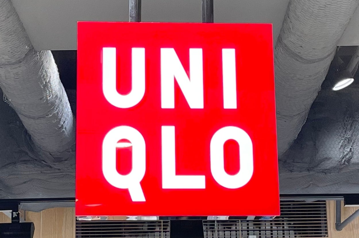 A Uniqlo store sign hanging from the ceiling with clothing shelves and price tags visible below