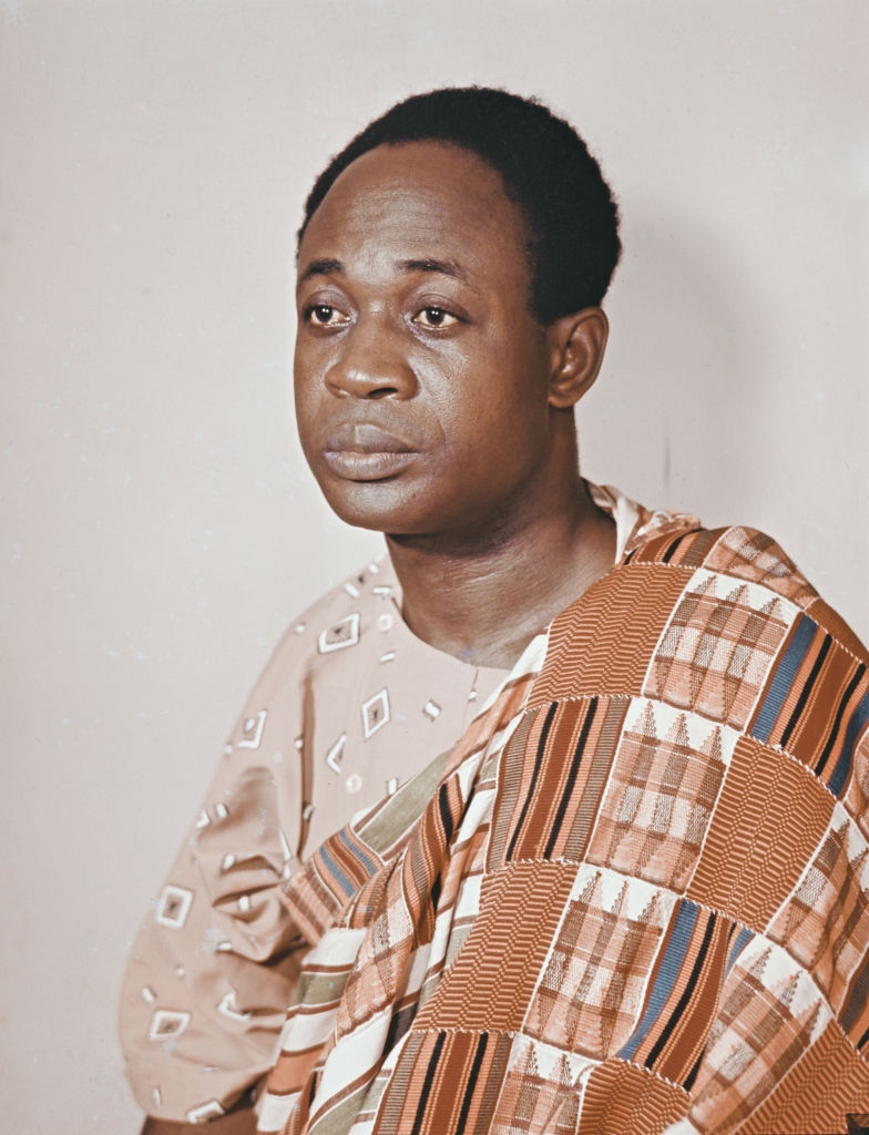 A person in a patterned traditional garment poses for a portrait, looking solemnly to the side