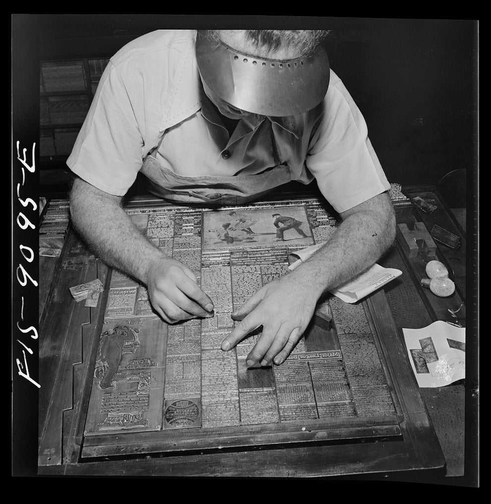 Person meticulously laying out newspaper pages for printing, using tools to align text and images on a grid