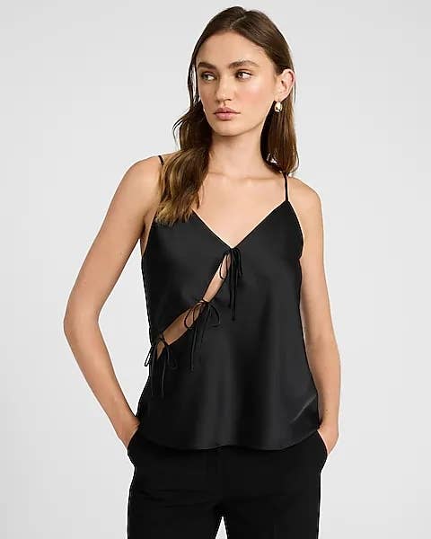 Person wearing a stylish satin camisole with necktie details and achromatic pants, posing against a plain background