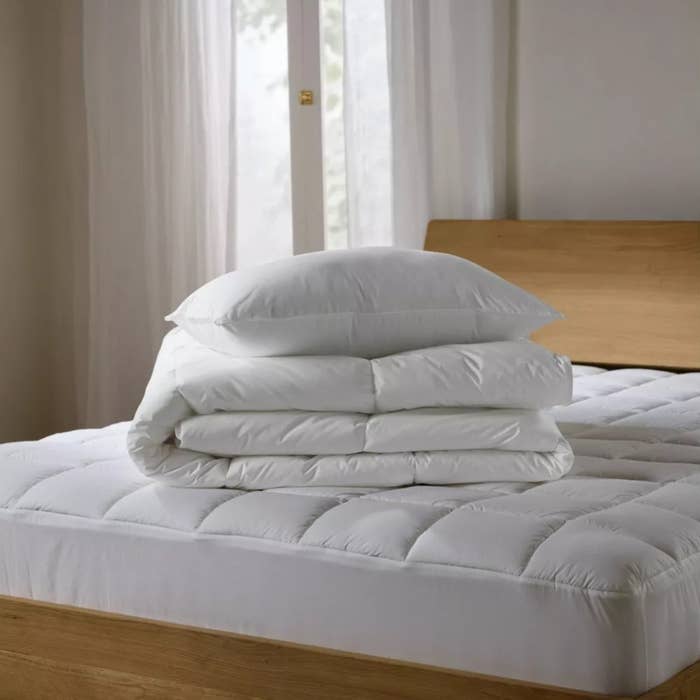 A neatly made furniture with stacked achromatic pillows and a folded duvet connected a quilted mattress, placed successful beforehand of ample windows