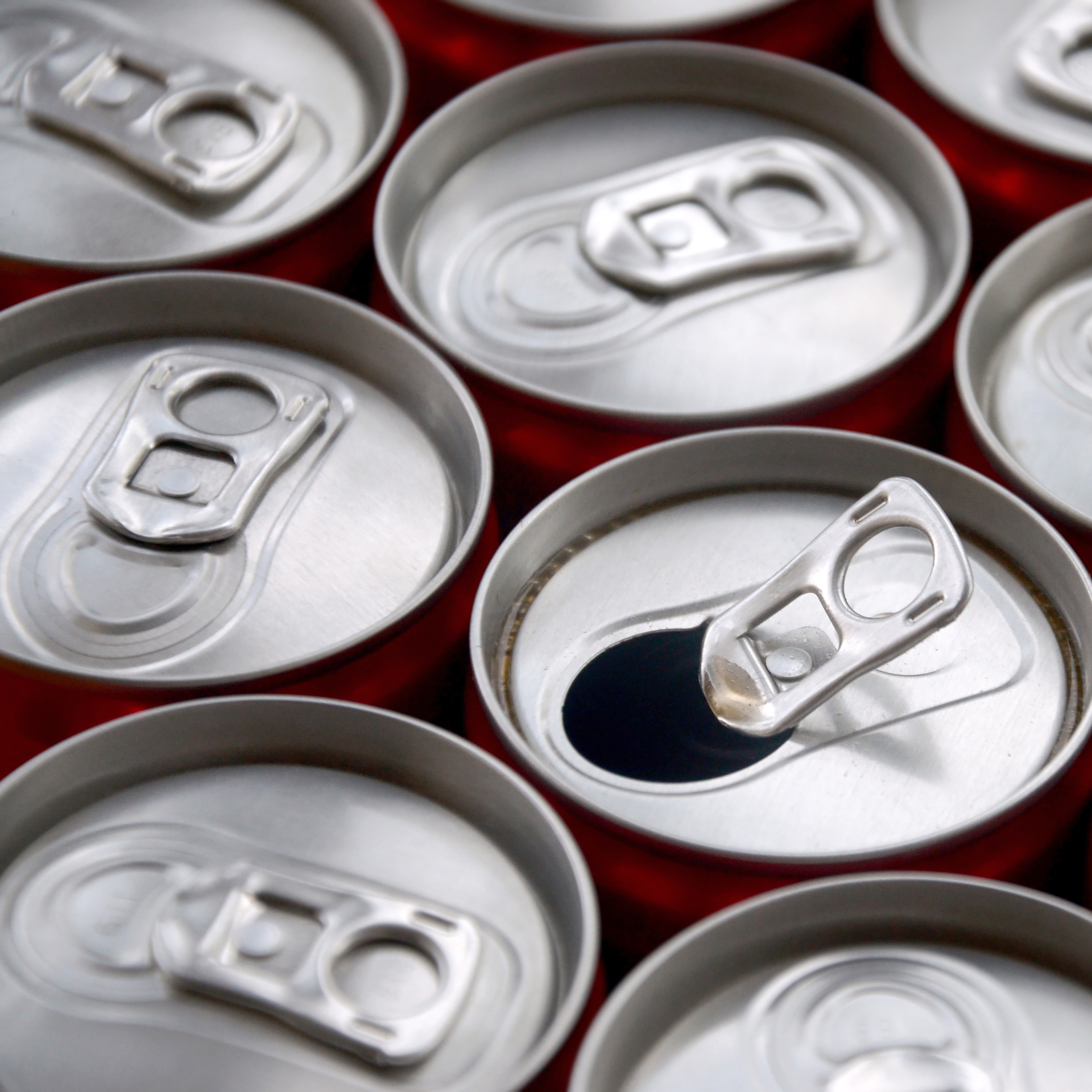 Open soda cans arranged closely together, one with the tab lifted, showing the open top