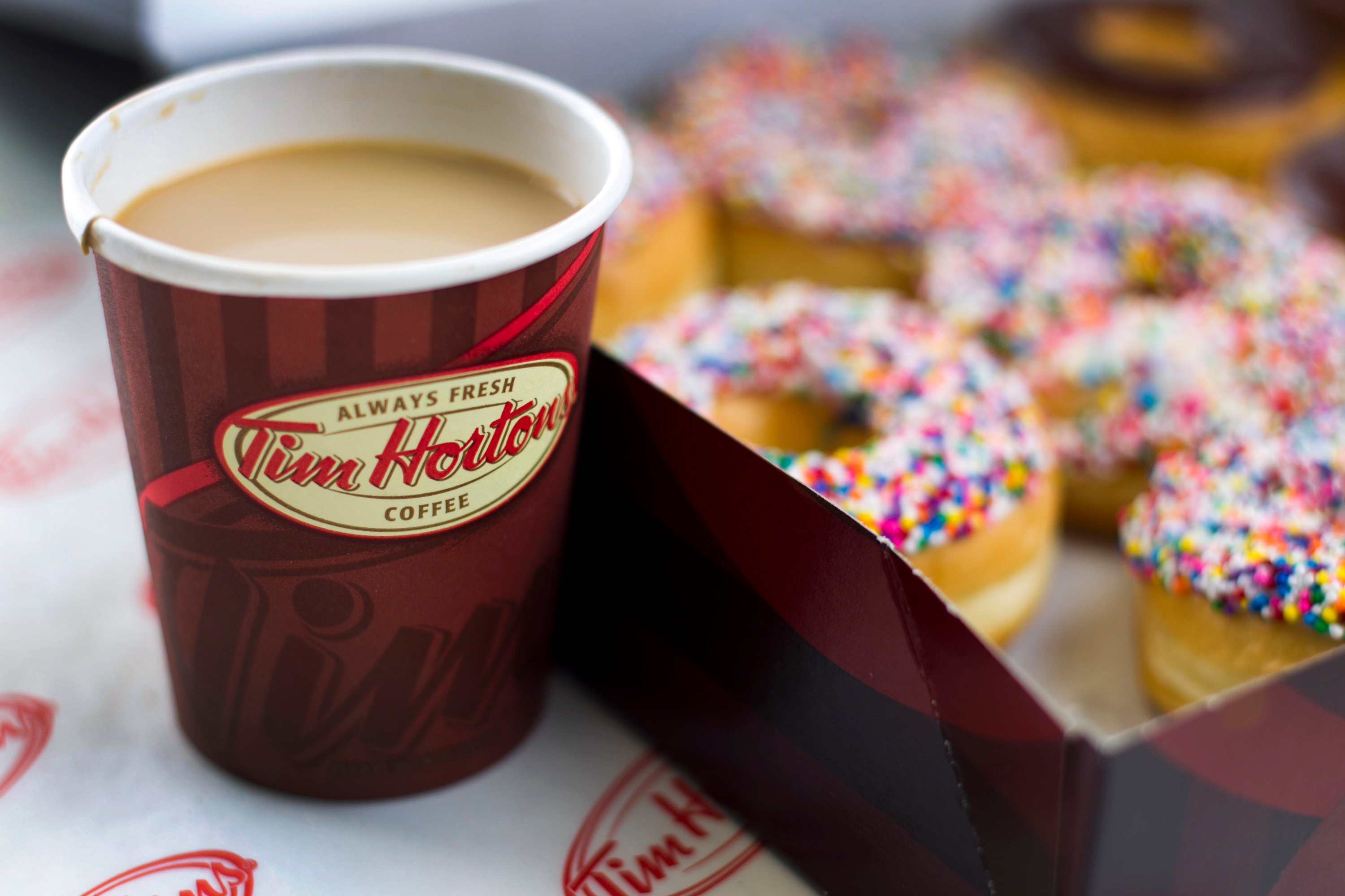 A cup of Tim Hortons coffee next to a box of donuts with colorful sprinkles