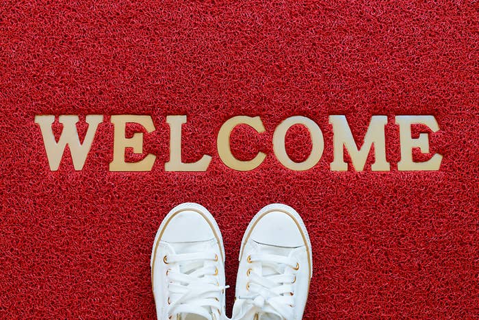 Pair of white sneakers on a red doormat with "WELCOME" spelled out in large letters