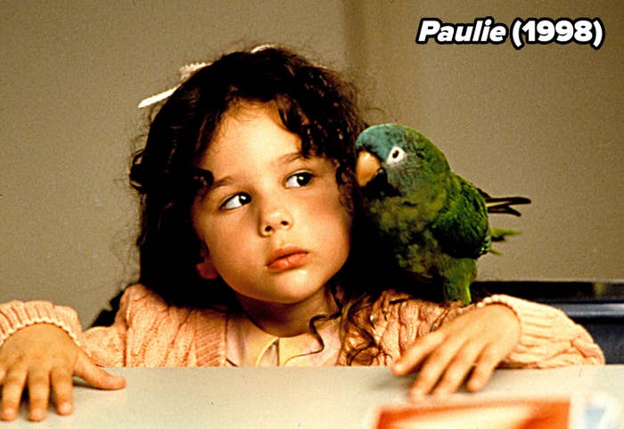 Young girl with curly hair looks at a green parrot on her shoulder, both appearing curious