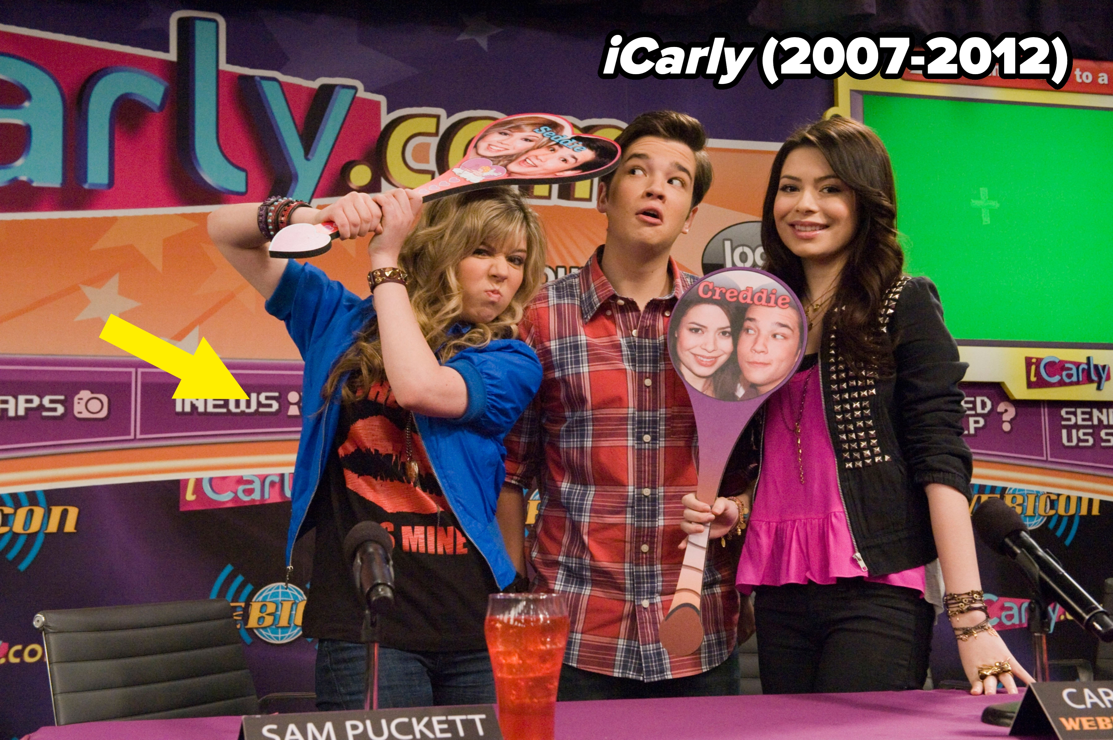 Three actors from a TV show at a promotional event. The two women are holding cutouts. They are dressed in casual, trendy outfits