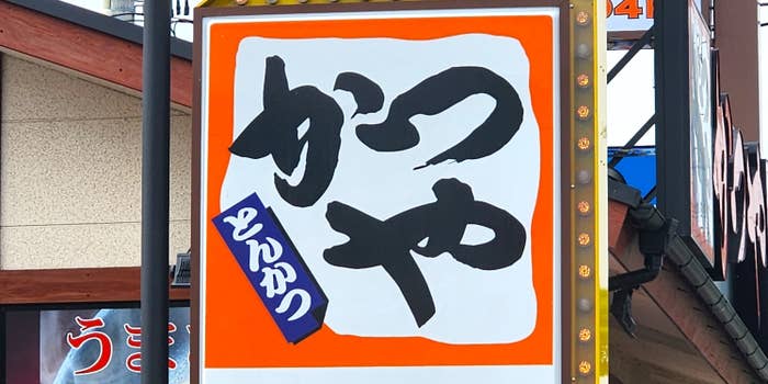 巨大な看板に「かつや」と大きく書かれ、その下に「とんかつ」の文字がある。