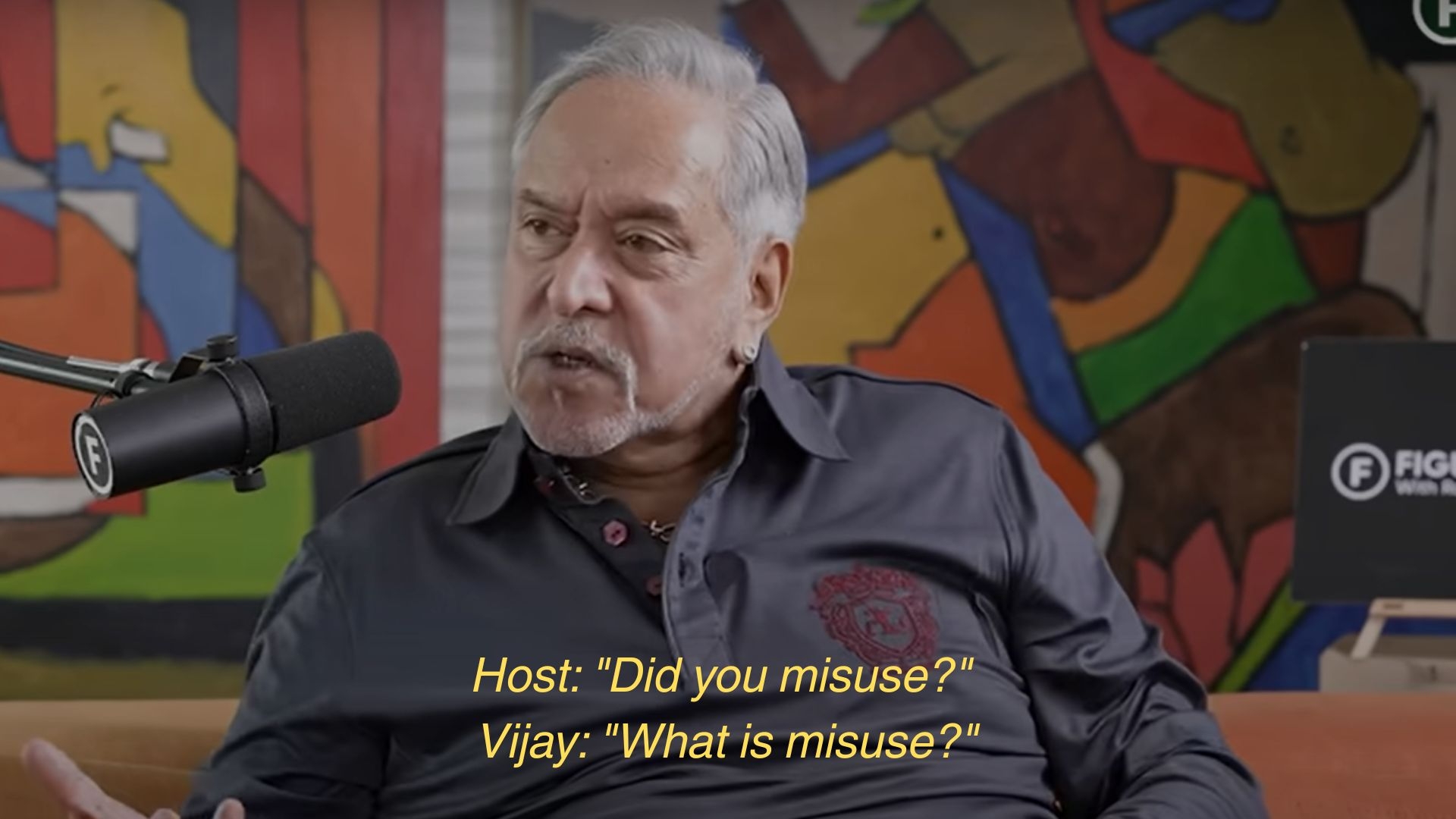 Man speaking into a podcast microphone with colorful abstract art in the background. Subtitles: Host asks about misuse; Vijay responds, "What is misuse?"