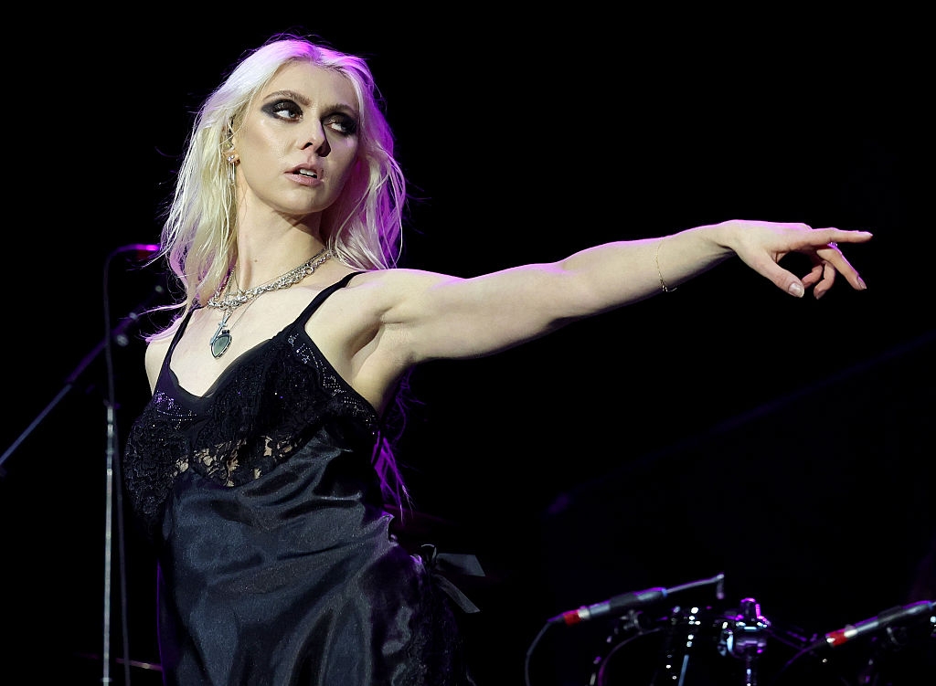 Person on stage in a black lace dress, pointing with an intense expression