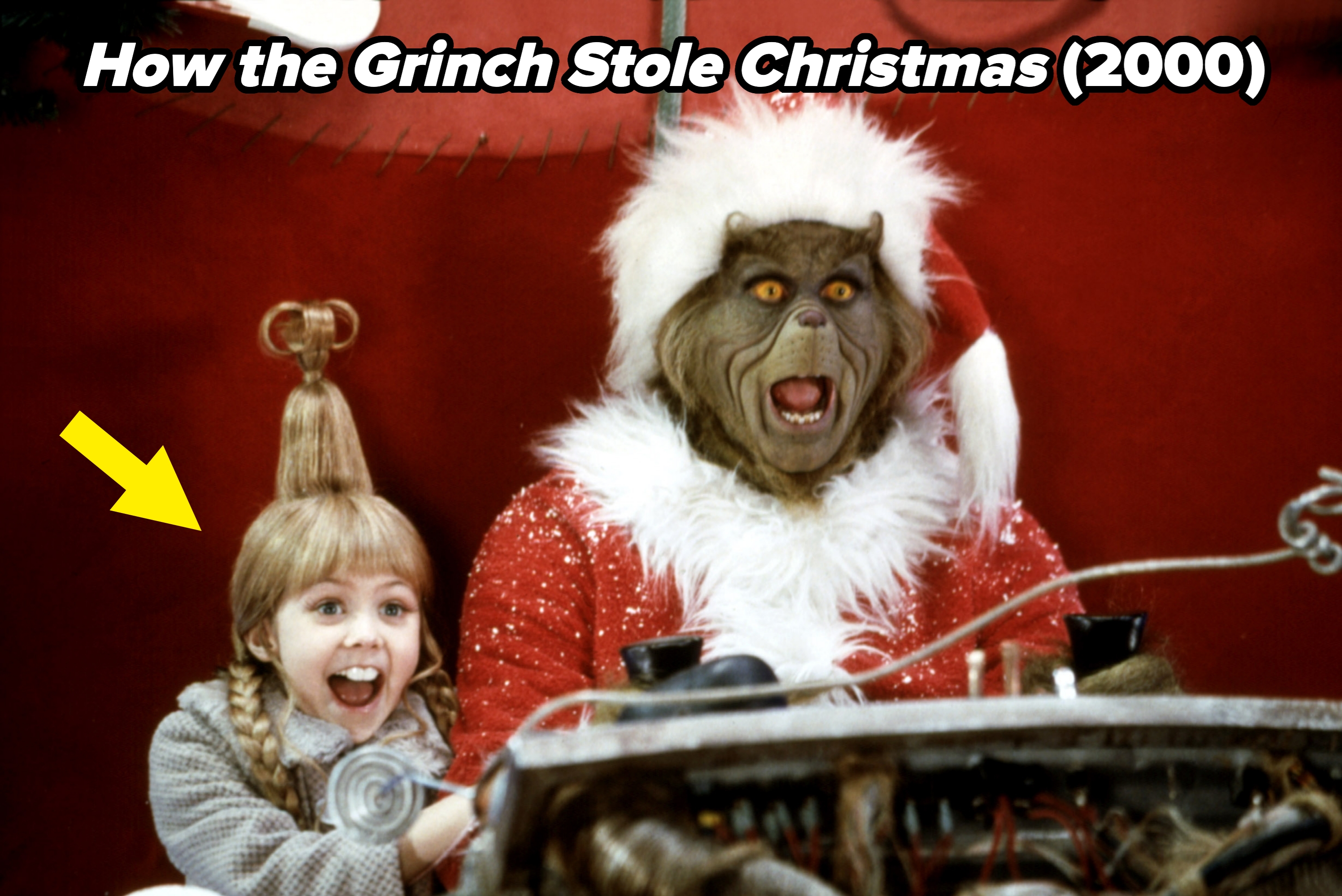 A girl with a unique hairstyle and a furry green character wearing a Santa outfit share a joyful moment in a festive setting