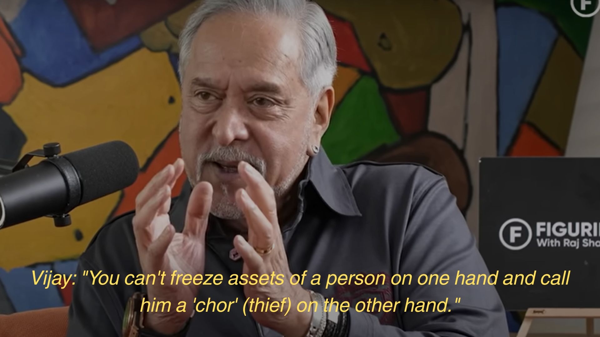 A person speaking into a microphone, gesturing with hands, with a quote about freezing assets and calling someone a thief
