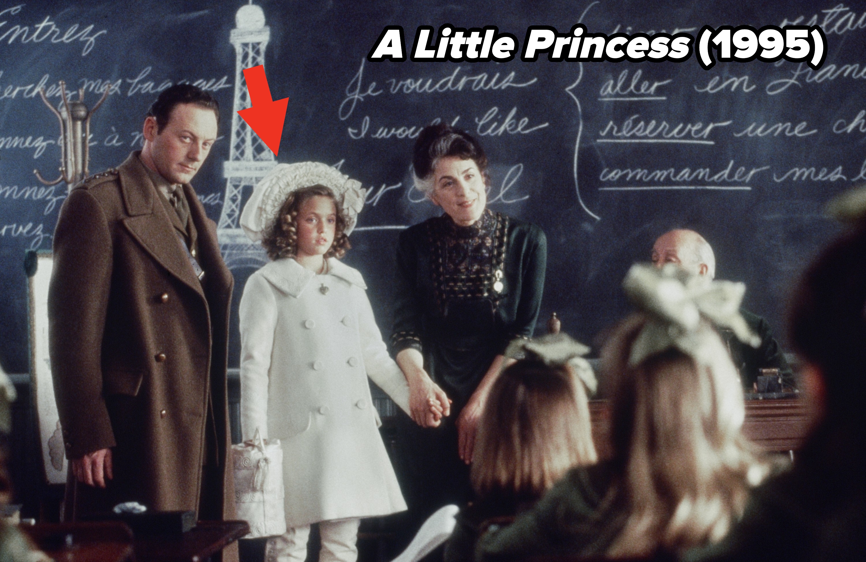 Scene from a period film showing adults and a child in a classroom with French words on the blackboard