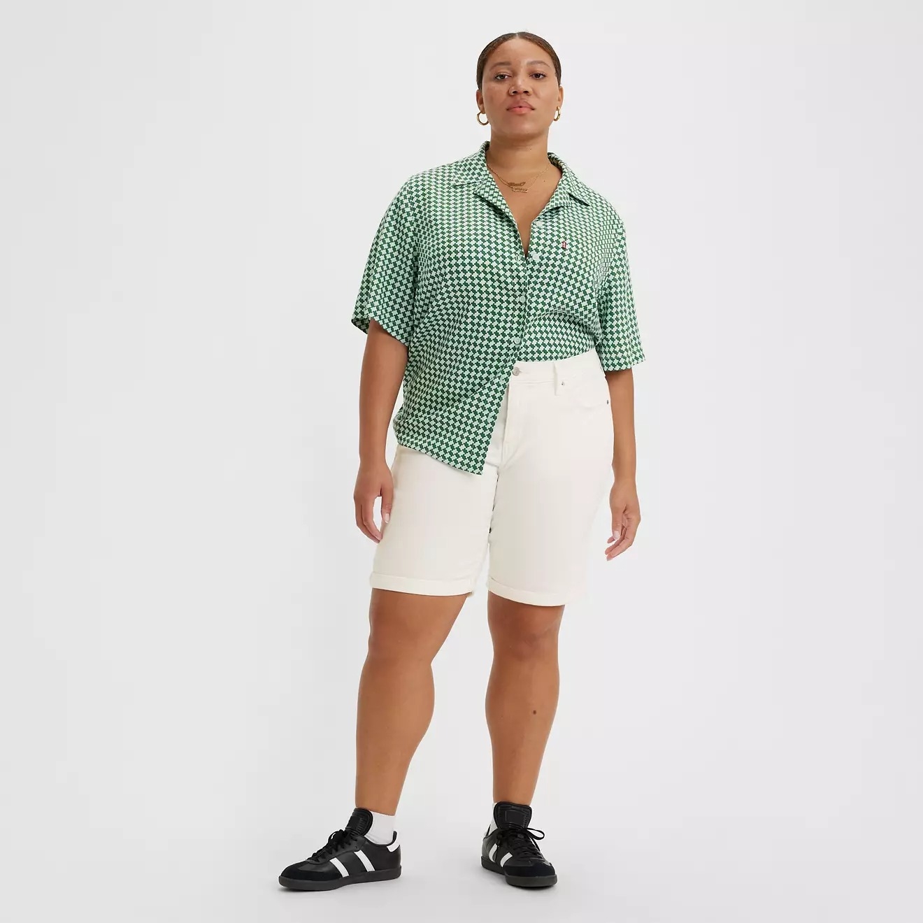 Person wearing patterned short-sleeve shirt, white shorts, sneakers, standing confidently against plain background