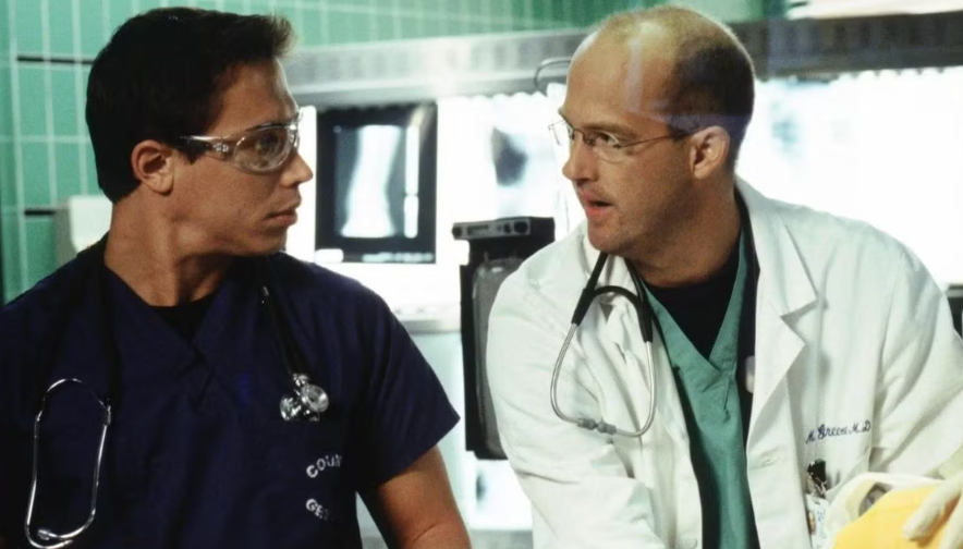 Two doctors in scrubs and lab coats converse in a medical setting, wearing stethoscopes around their necks