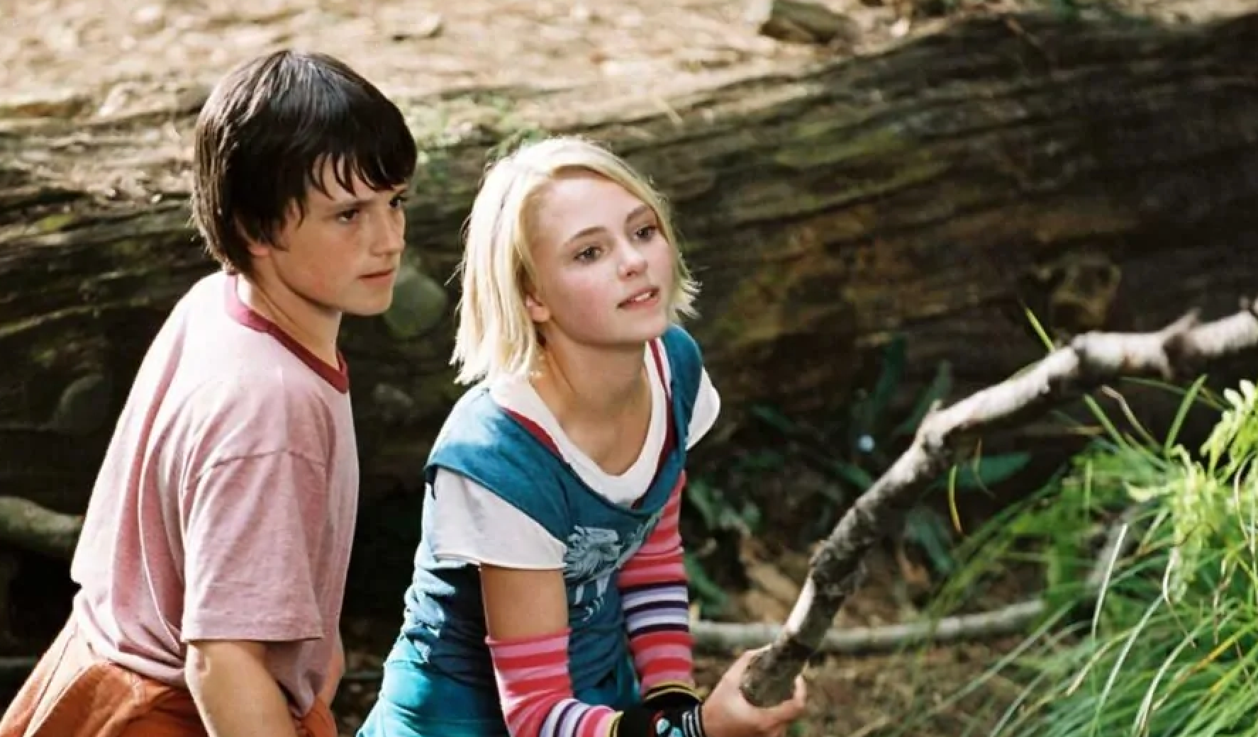 Two young individuals outdoors, holding a stick. They are appearing focused and engaged in their task