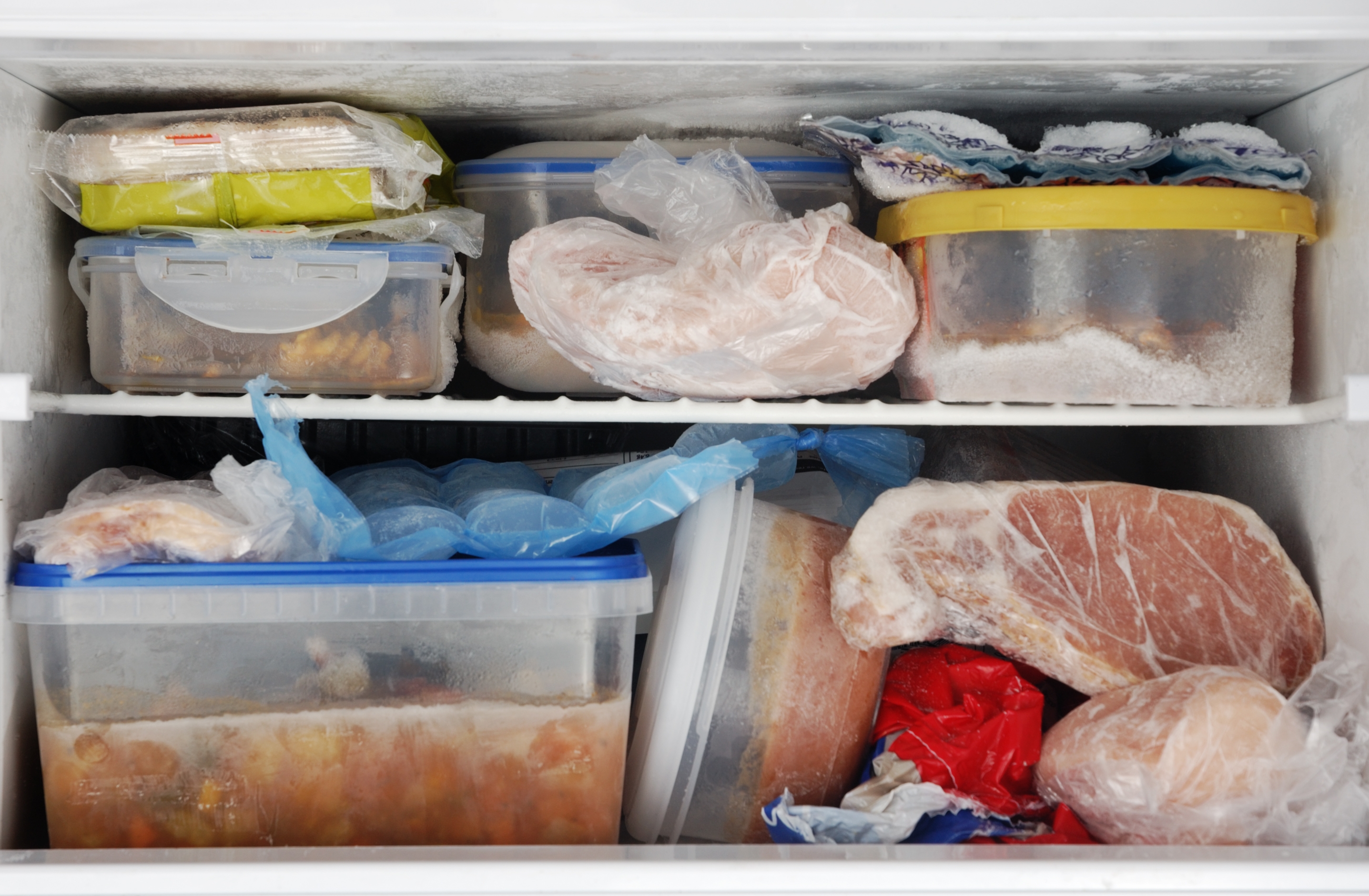 Freezer packed with various frozen foods in containers and bags, including meats and prepared meals, stacked on two shelves
