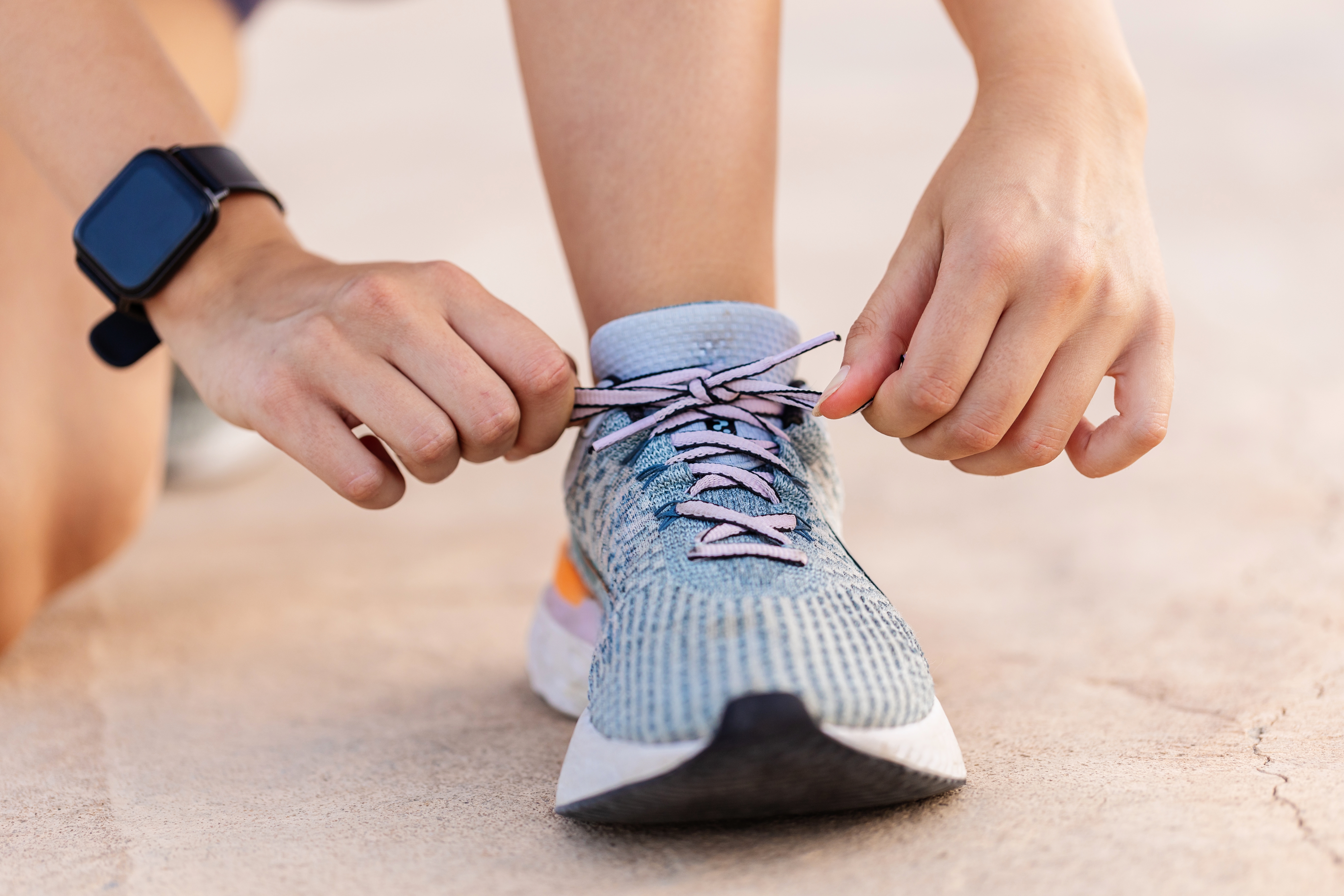 Person tying the laces of a running shoe with a smartwatch on their wrist, preparing for exercise