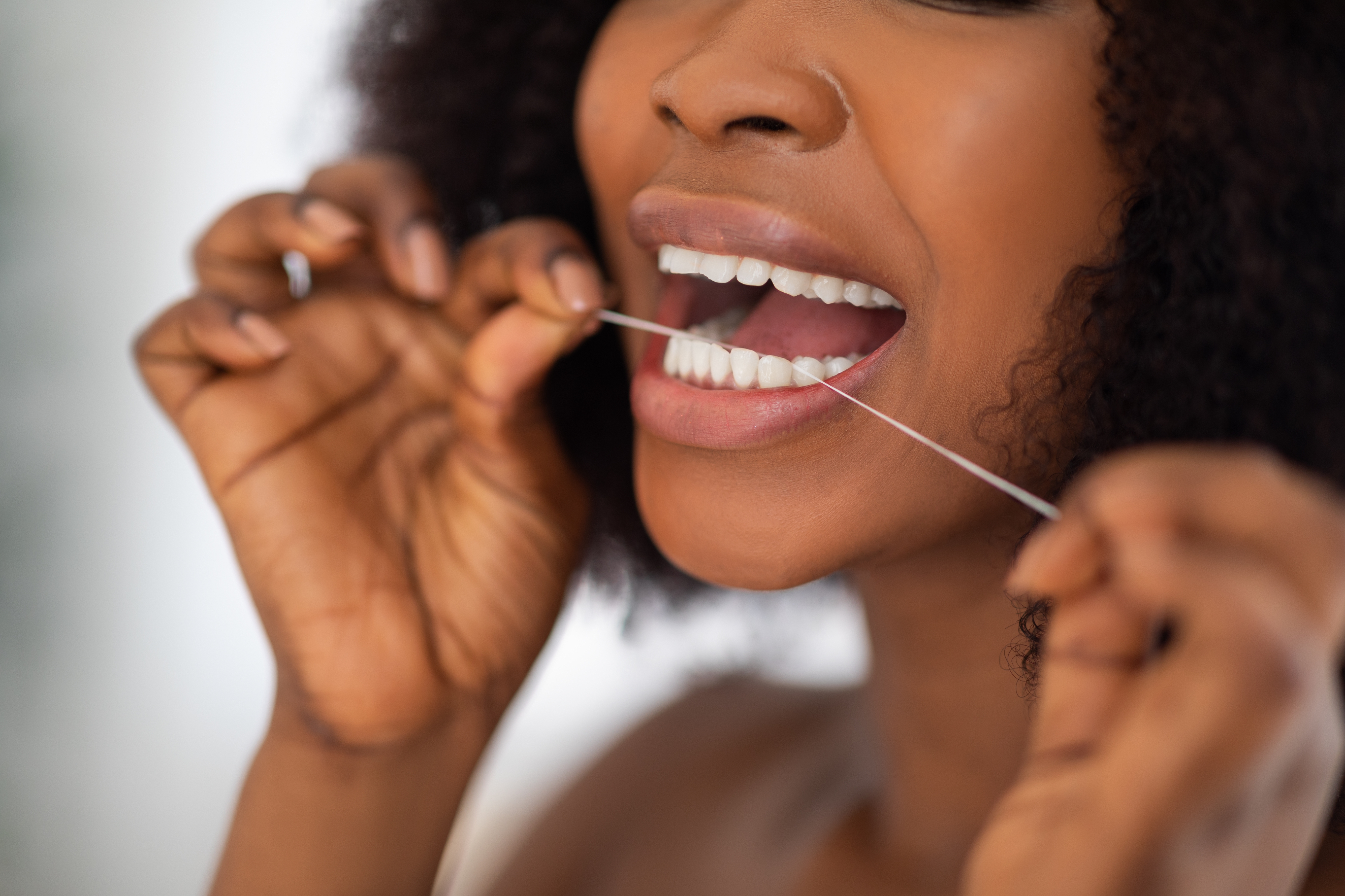Person flossing teeth, showing a close-up of their mouth and hands holding the floss, demonstrating dental care