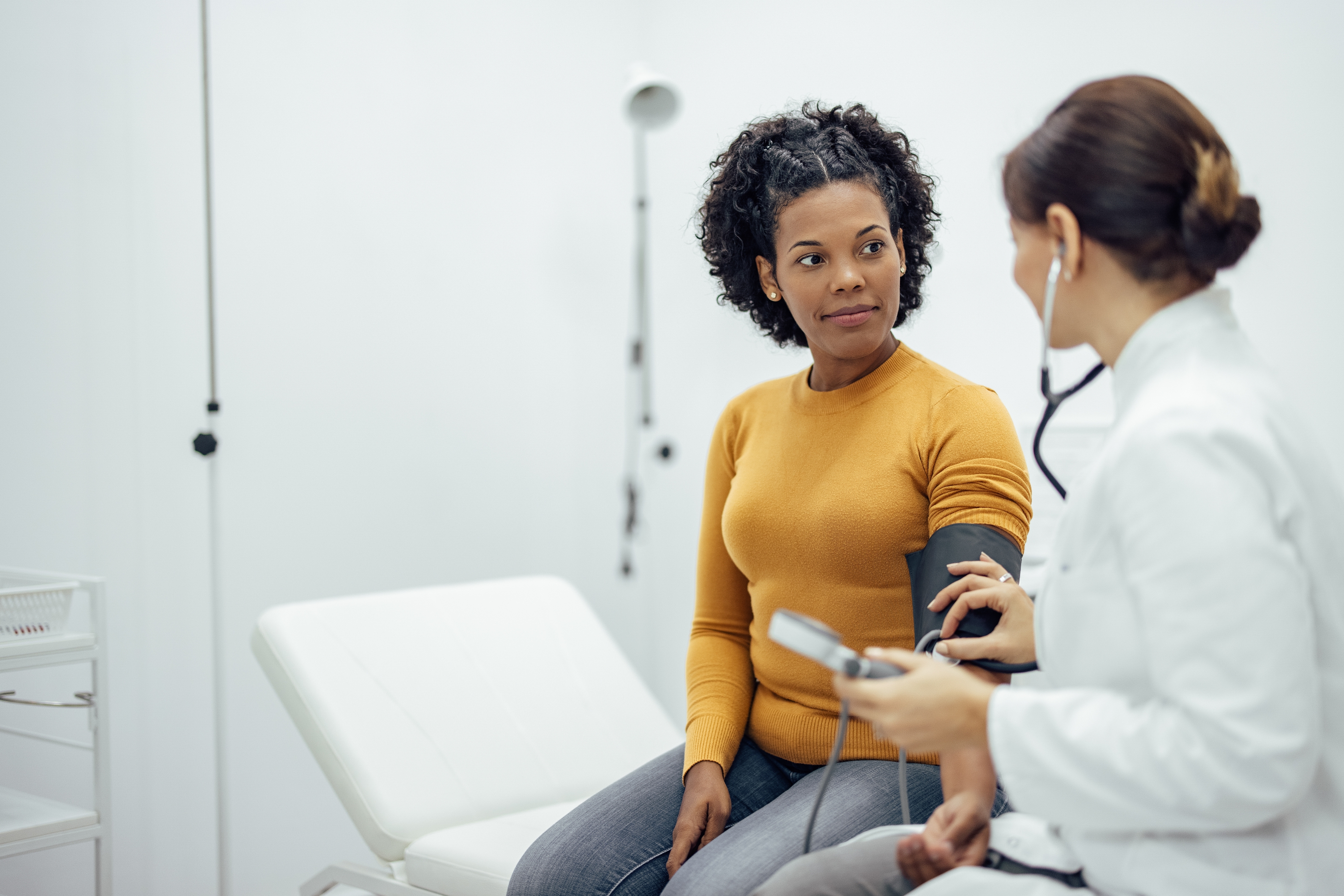 A healthcare professional checks a patient's blood pressure in a clinic. The patient sits on an examining table