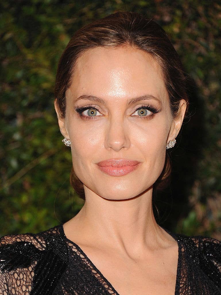 A person with styled hair and elegant jewelry, wearing a detailed, sophisticated gown, poses at an event