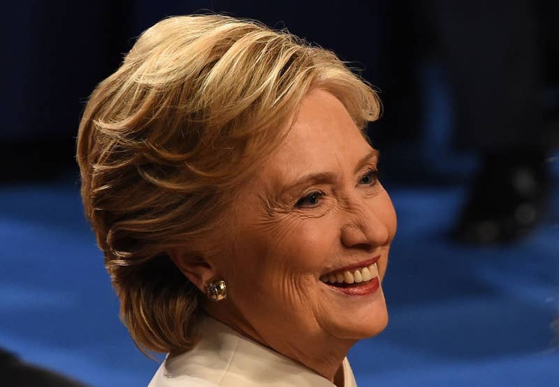 A person smiling at an event, wearing a white outfit and pearl earrings, with short, styled hair