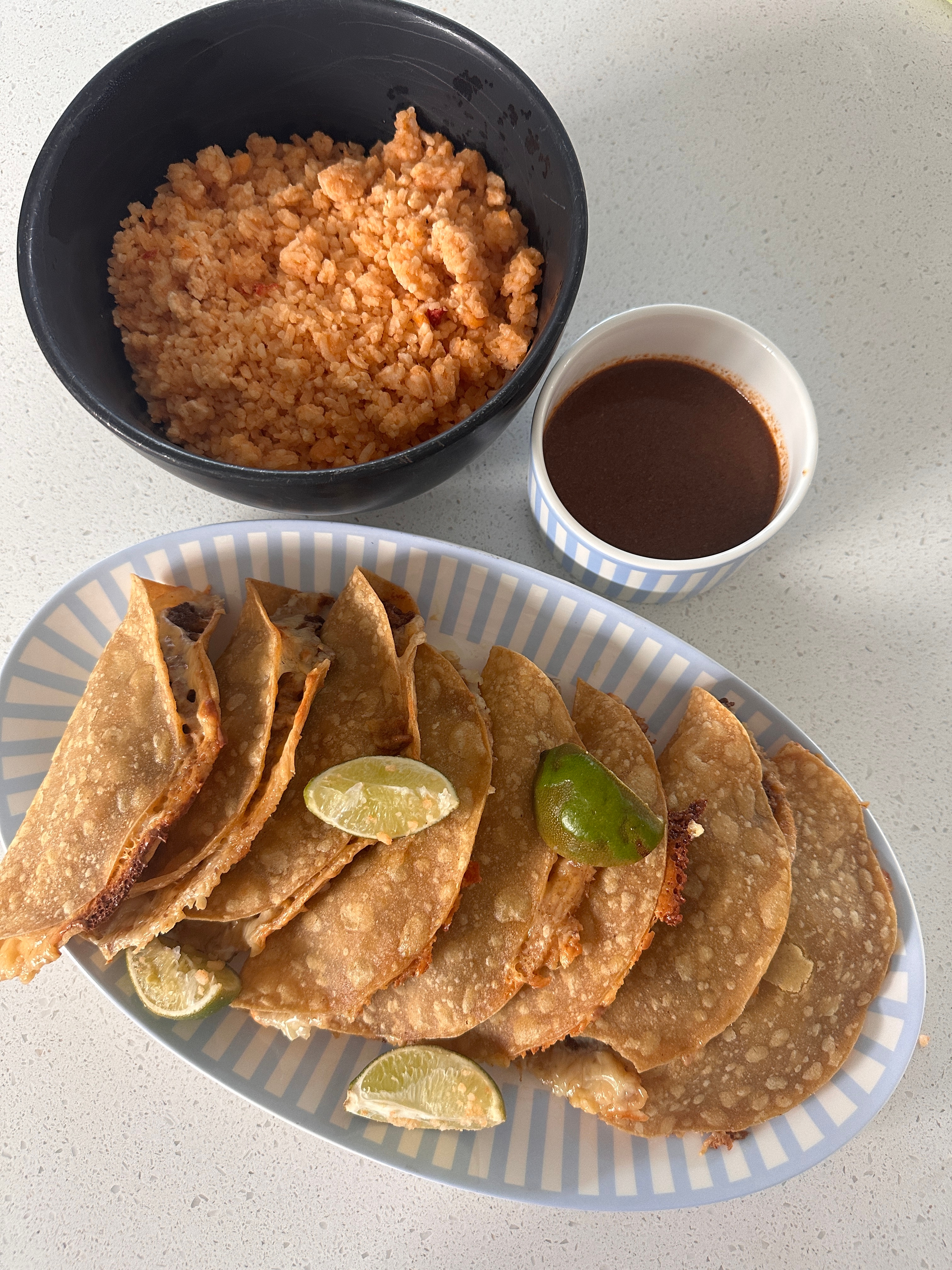 Plate of crispy tacos with lime wedges, served with a bowl of rice and a cup of sauce