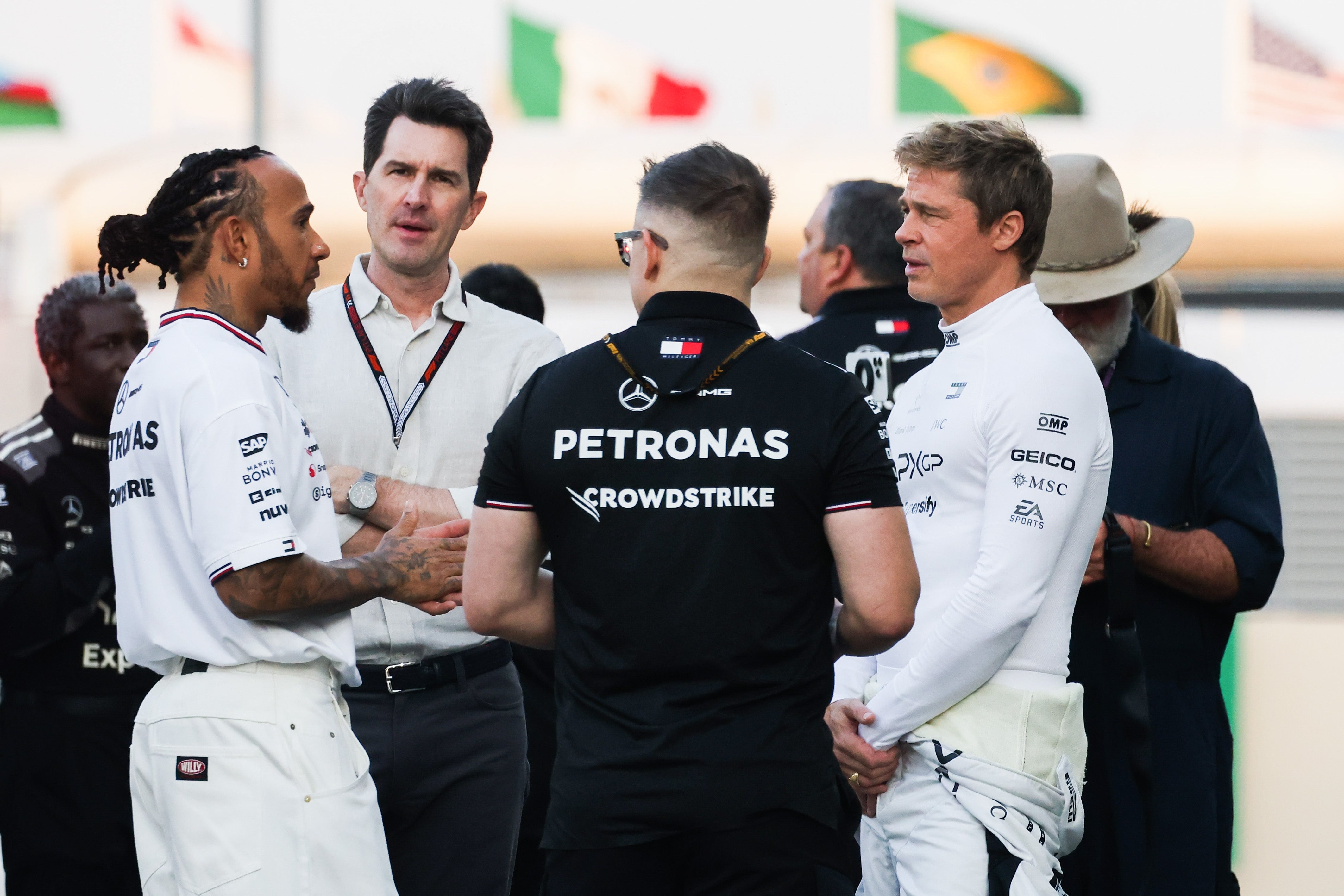A group of individuals, including a race car driver in a white suit, casually converse at an outdoor event, possibly related to racing