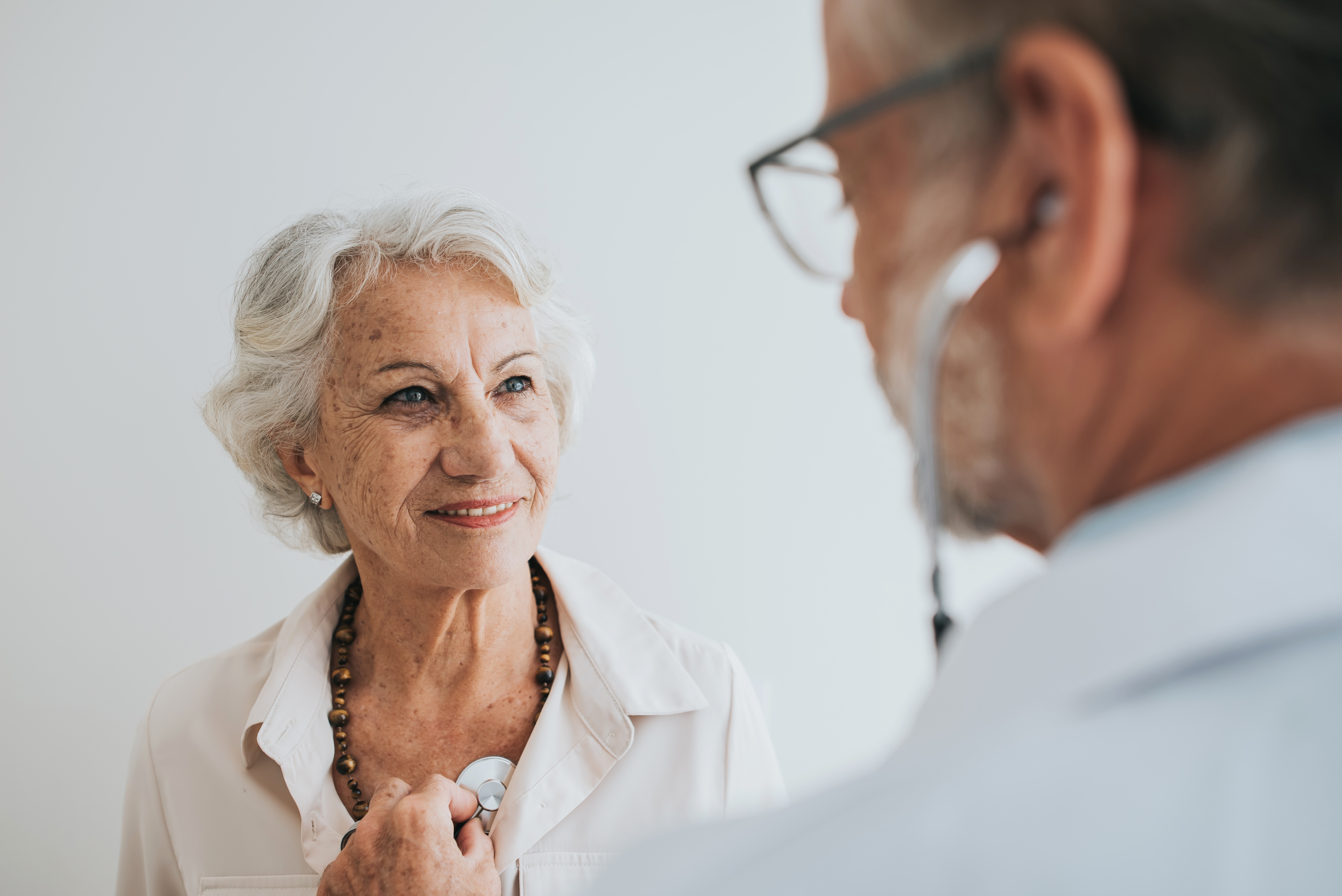 Eldre kvinne smiler mens en lege bruker et stetoskop for å lytte til hjerteslaget hennes, og formidler en følelse av omsorg og helseundersøkelse