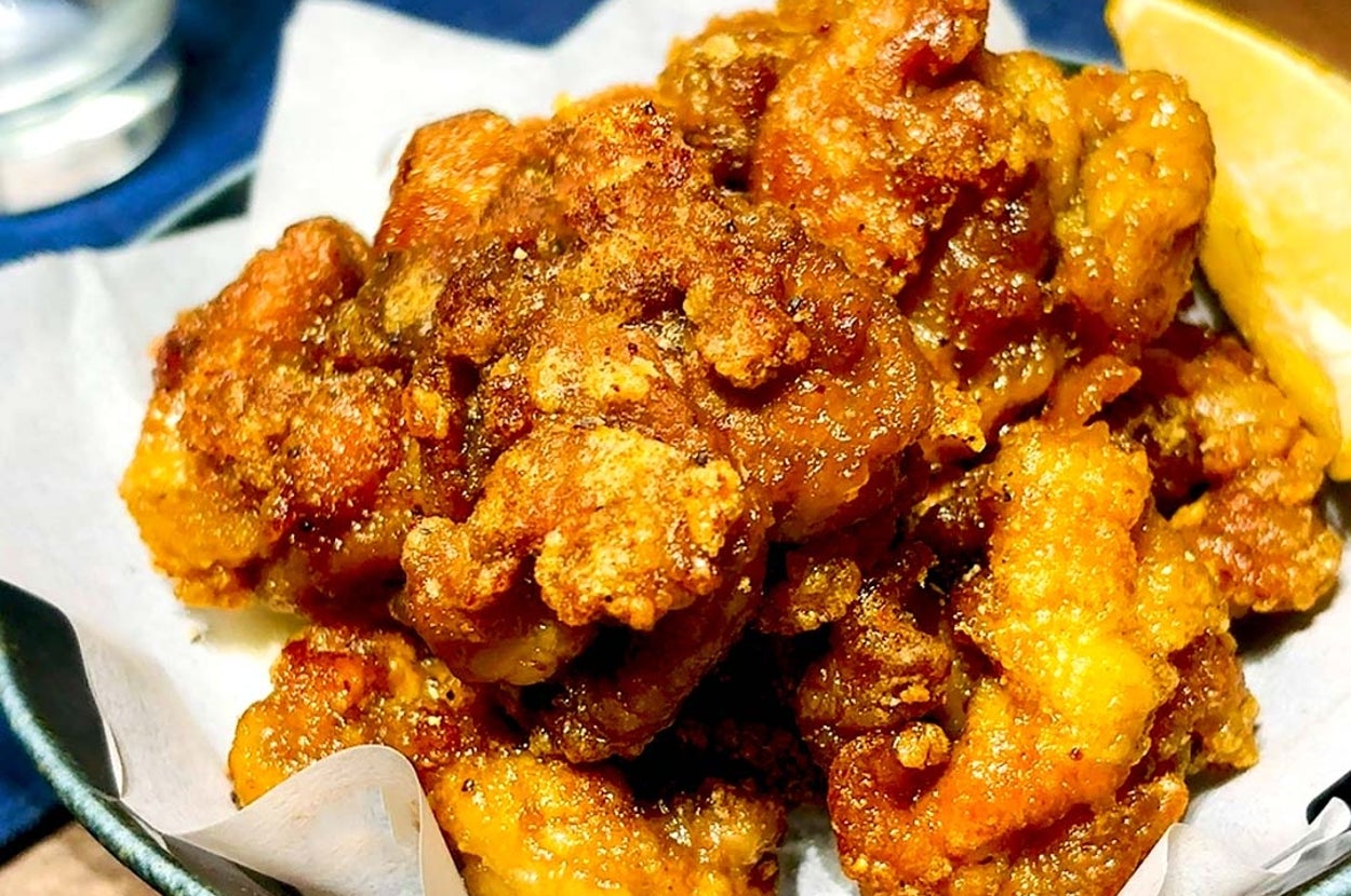 唐揚げが白い紙の上に盛られ、横にレモンのくし切りが添えられたおいしそうな料理。