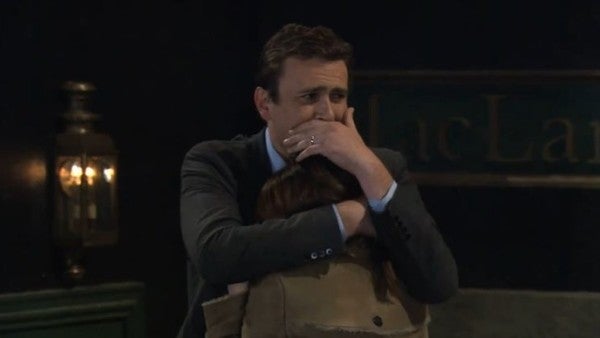A person in a suit, looking emotional, comforts someone in a brown jacket during an intense scene